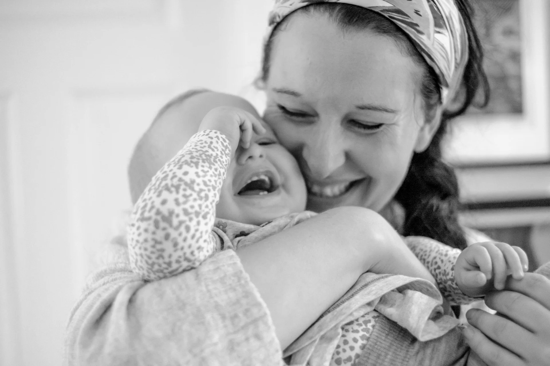 Mor holder baby i armene, og gir henne en god klem. Begge smiler og ler.