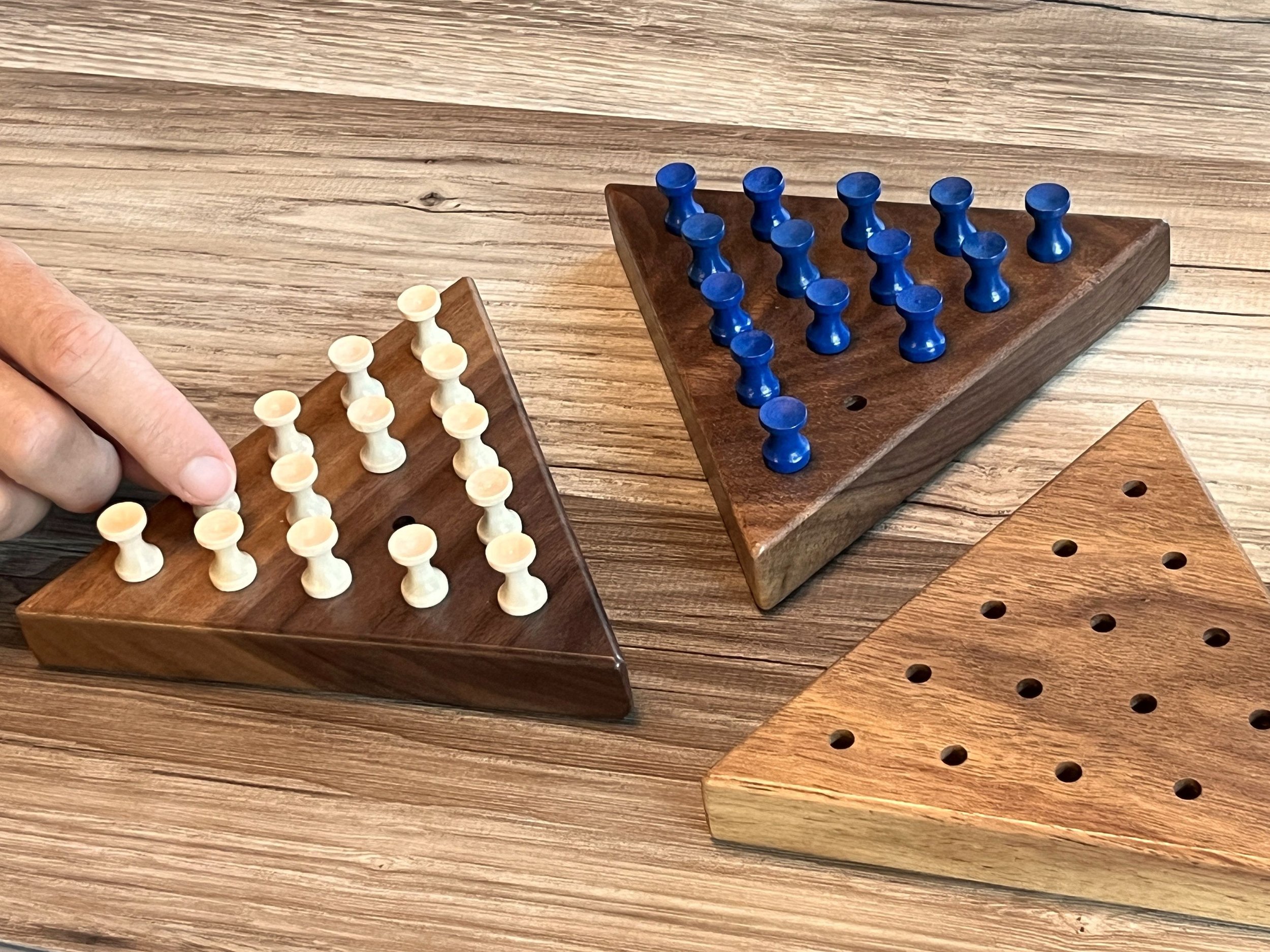 The picture shows a person's hand taking one peg out of a triangle peg solitaire board.