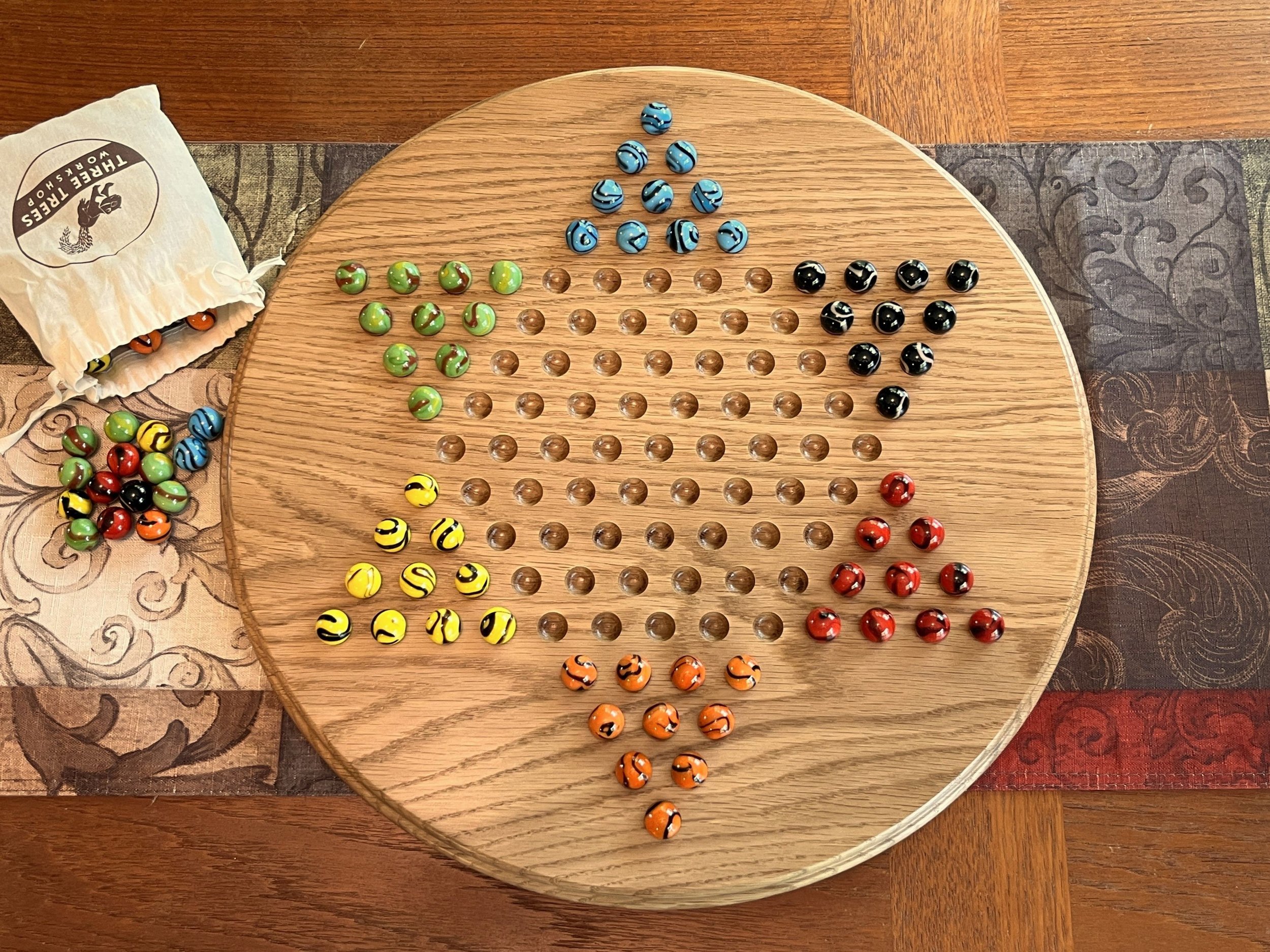 Chinese checkers board made from solid oak, shown with colorful glass marbles and the small bag to hold marbles off to the side.