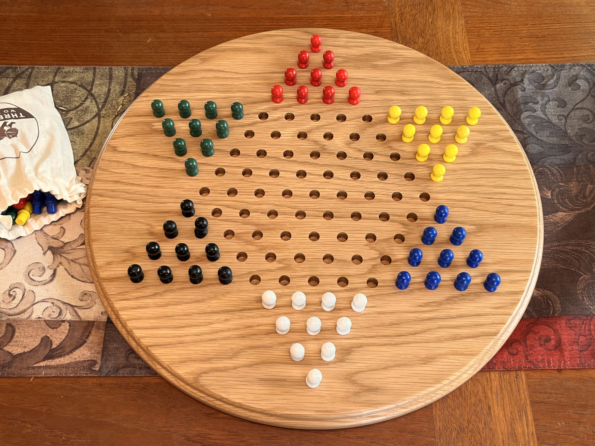 Solid oak Chinese checkers board displayed on a table with six colors of painted wooden pegs.