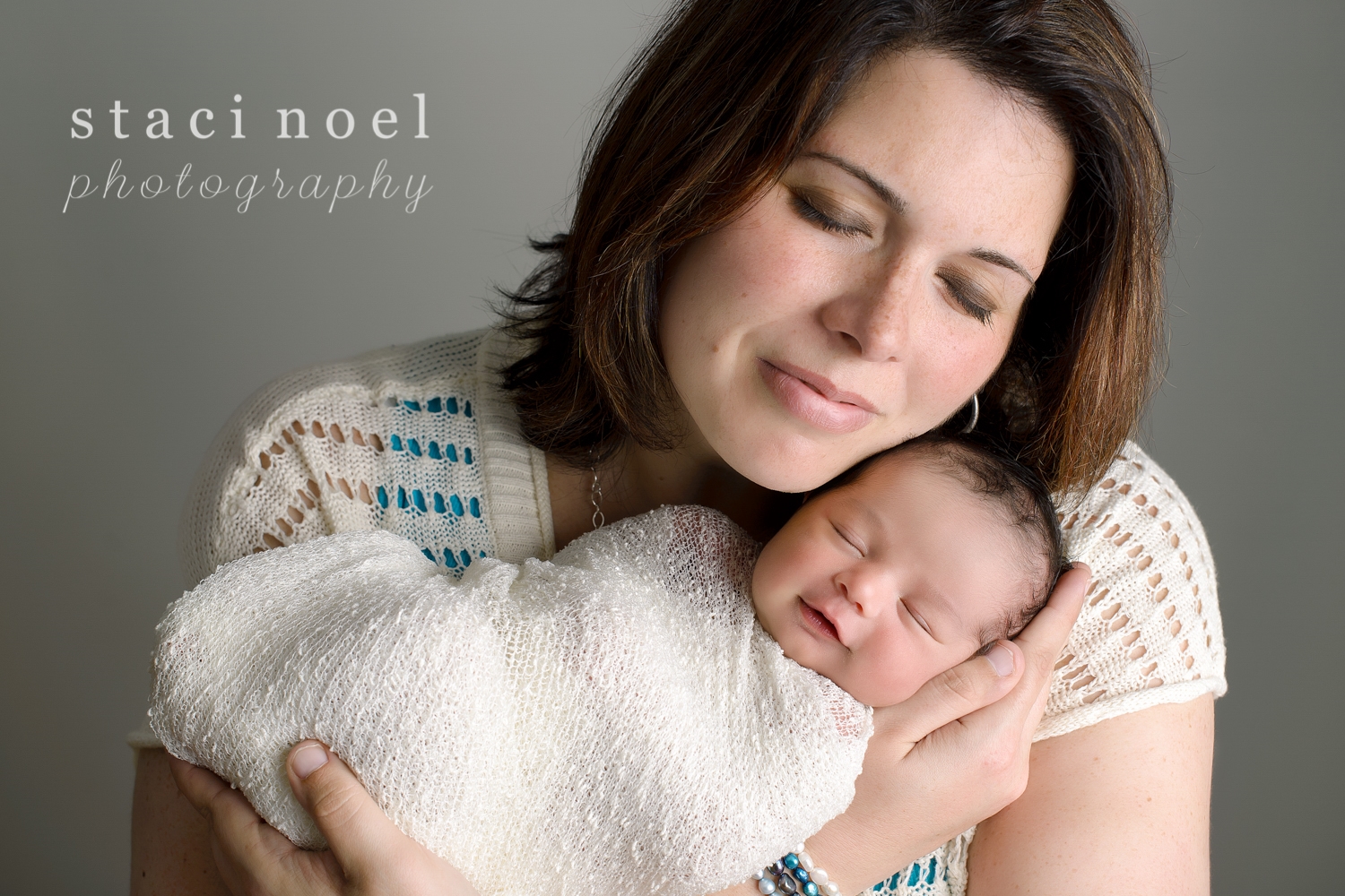 Harrisburg NC newborn baby girl photographed in her mothers arms smiling on a grey wall by Staci Noel Photography