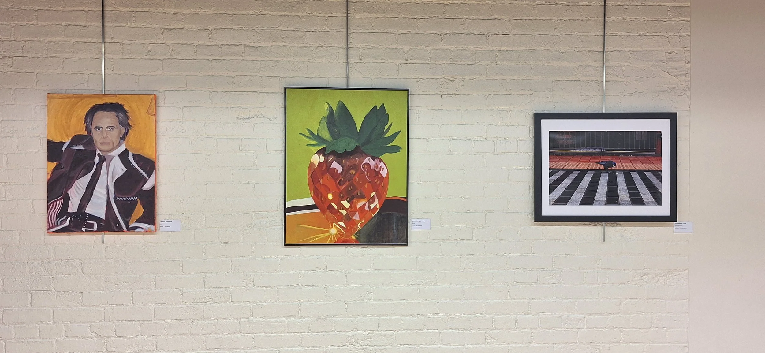Gallery Wall displaying an oil painting portrait, a strawberry still life painting, and photograph of a crow in a city street