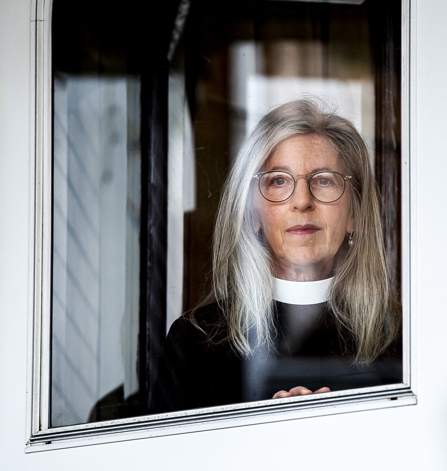 “So much of our life of faith, it comes to life in our voices,” said Rev. Amy Schifrin, associate professor of liturgy and homiletics at Trinity School for Ministry, seen here posing for a portrait through a window of her home, Thursday, May 14, 202