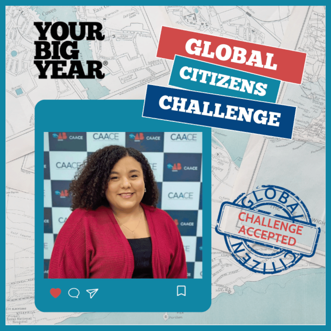 A woman with curly hair in a pink blazer smiling at the camera, standing in front of a CAACE backdrop at a professional event.
