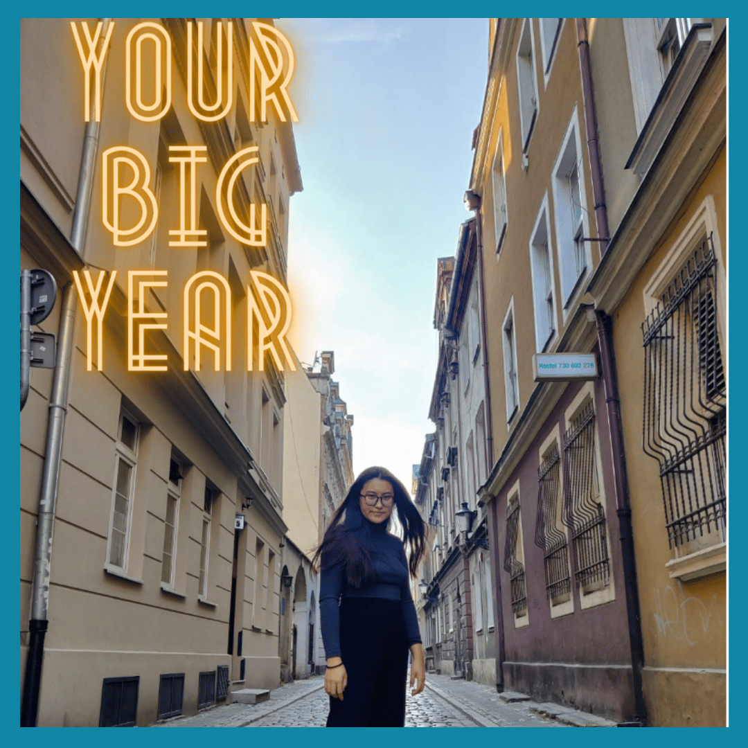 A woman standing in a narrow European-style street with old buildings on either side. Text overlay says 'YOUR BIG YEAR' in large, neon-style letters.