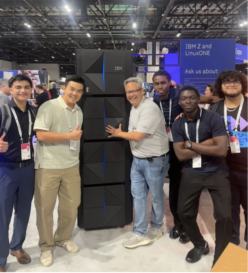 Group of five men standing in front of an IBM Z and LinuxONE server at a technology conference.