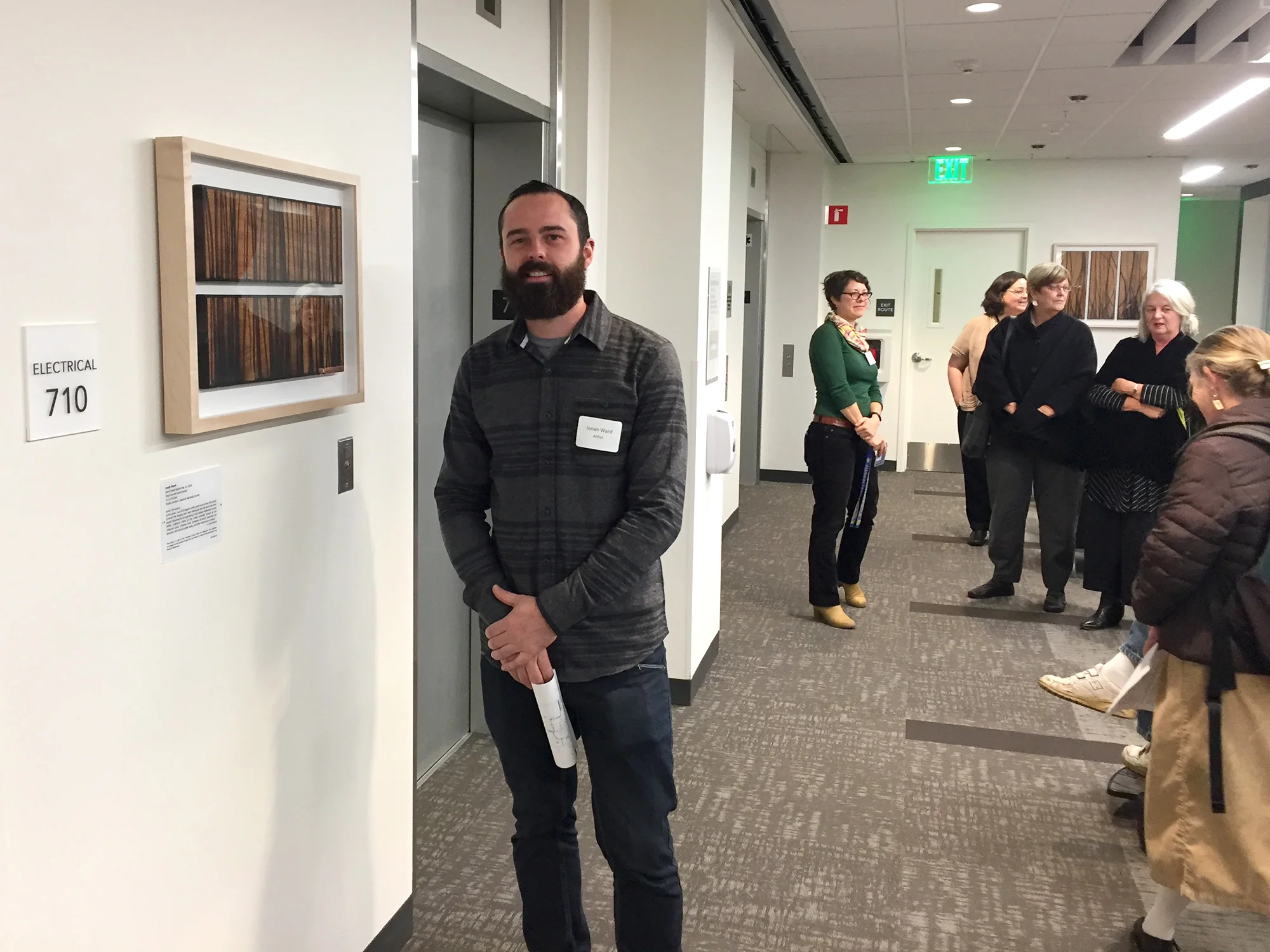 Jonah Ward stands next to another one of his permanently installed glass burned panel pieces during the artist walk-through. The other piece can be seen in the back right.