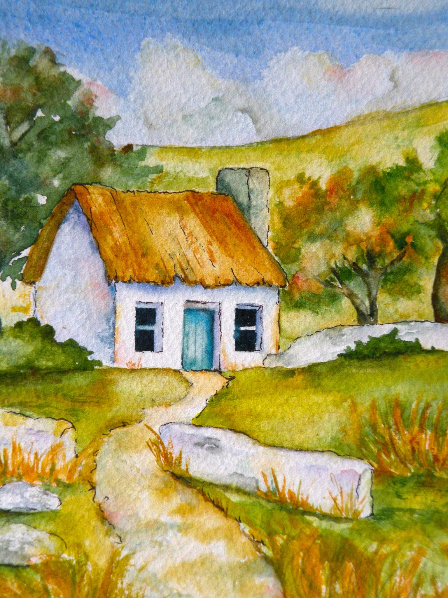 A path leads to an Irish cottage with a thatched roof.  The colors are autumn colors set against a blue sky.