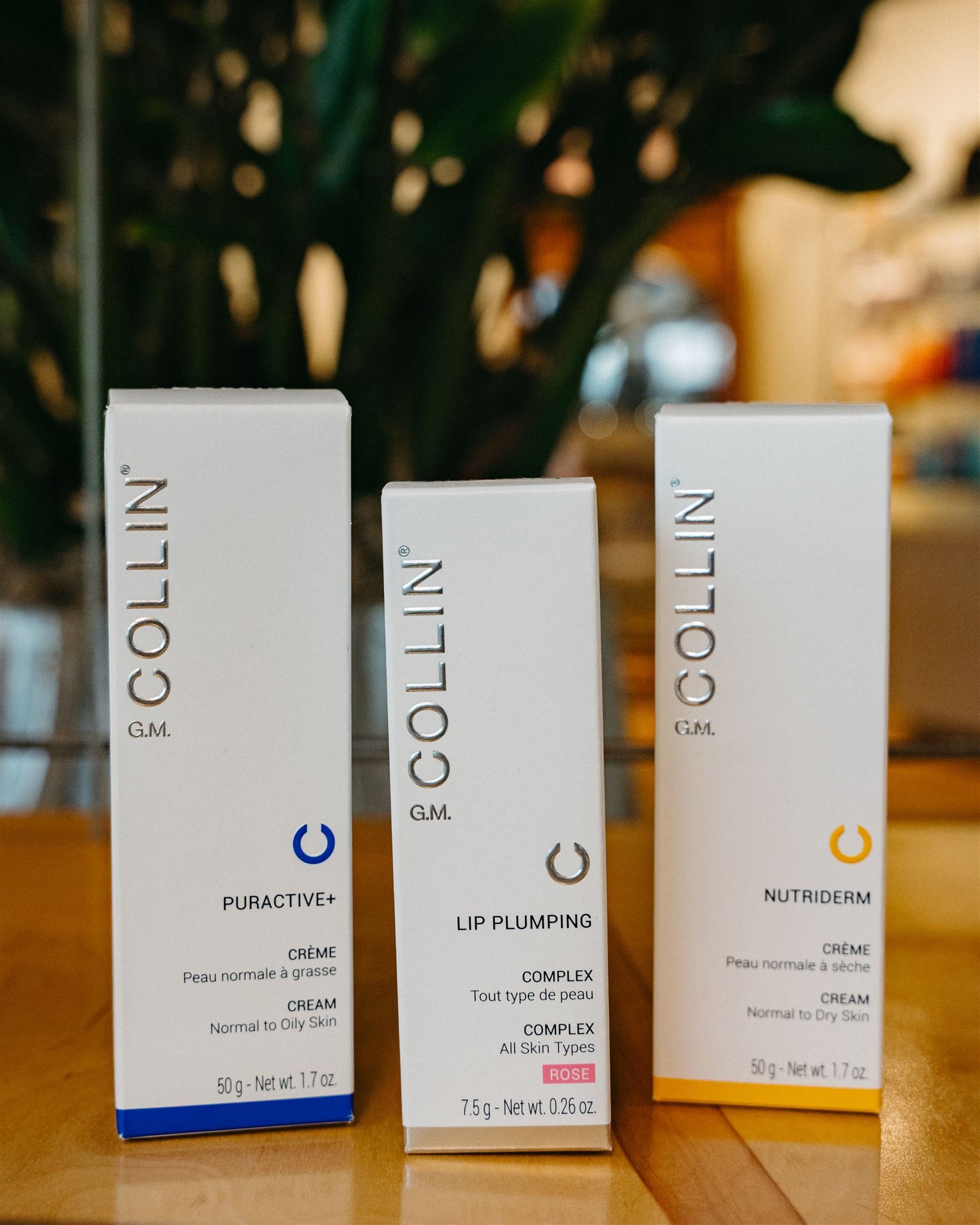 G.M. Collin skincare products including Puractive+ cream for normal to oily skin, Lip Plumping Complex for all skin types, and Nutriderm cream for normal to dry skin, displayed on a wooden surface with a blurred background.