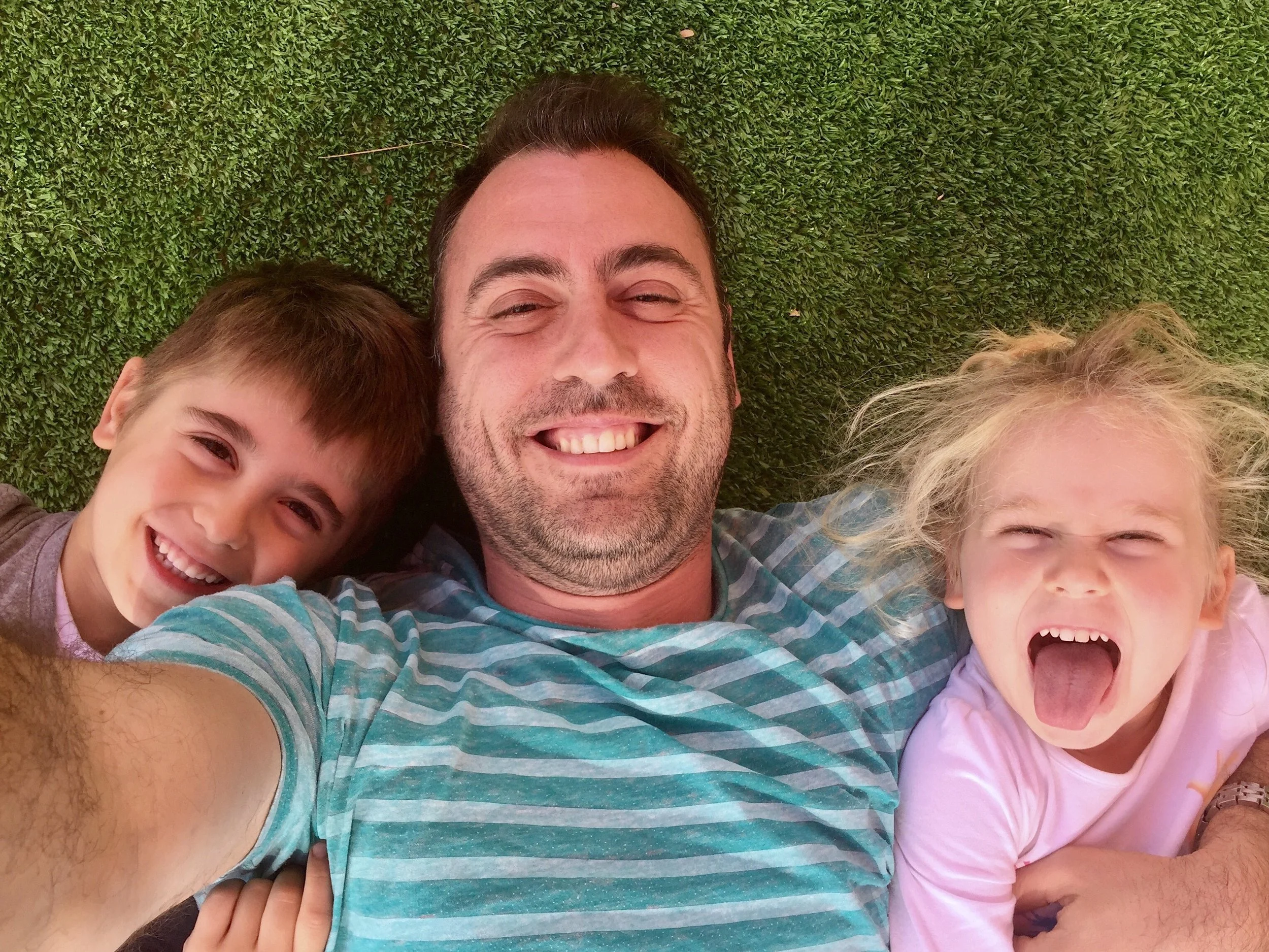 Family Fun: Smiling Dad and Silly Kids Taking Selfie on Turf - Garden City Dental Wellness