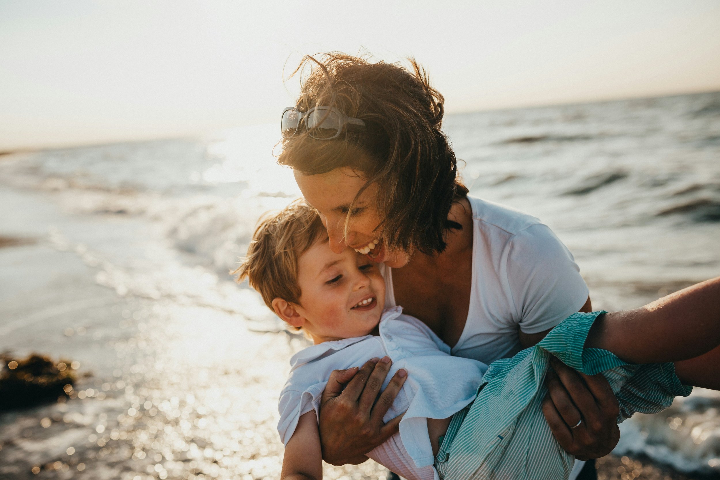 Beachside Smiles: Joyful Mom Holding Son on the Beach - Garden City Dental Care