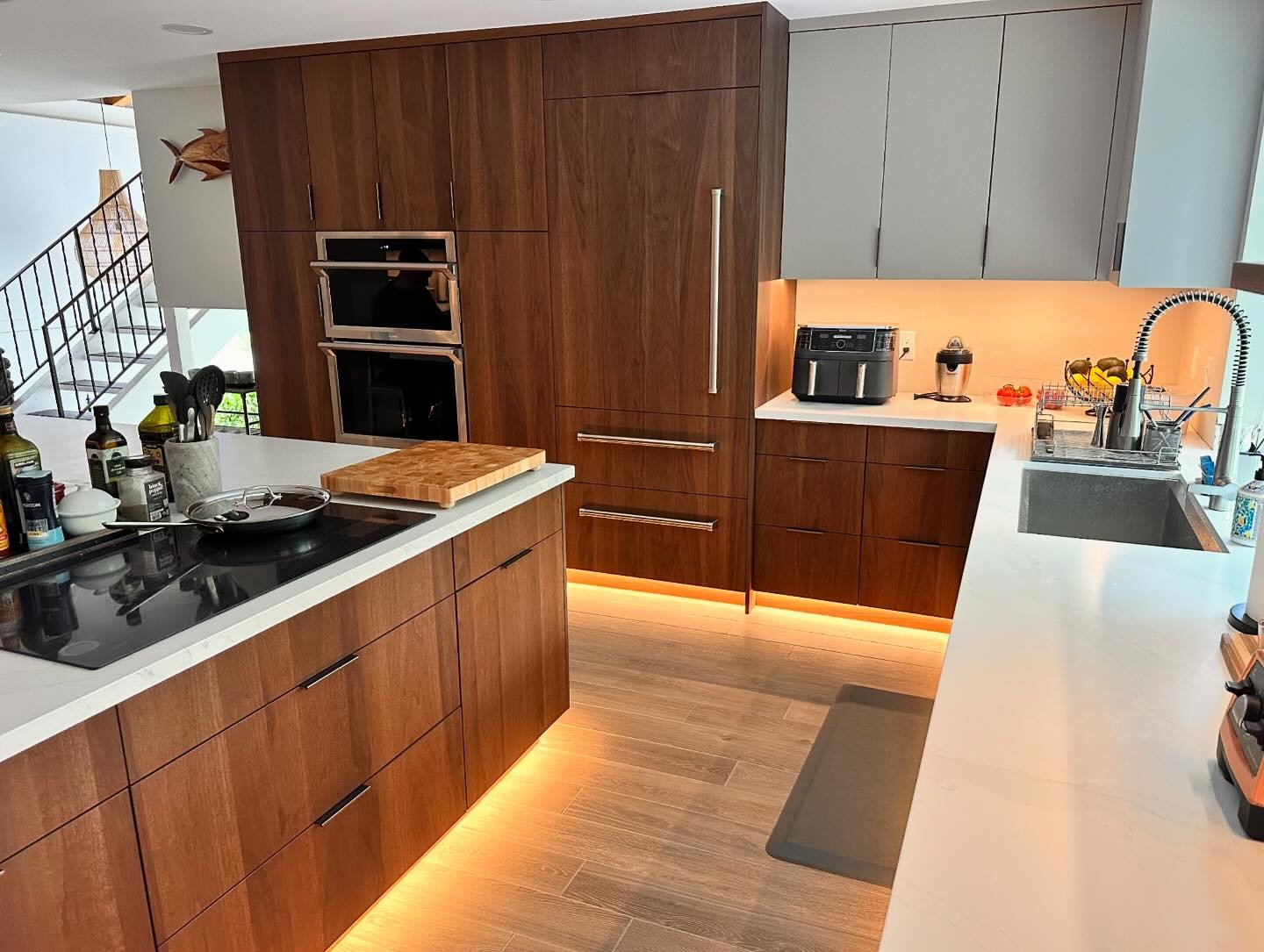 An open-concept kitchen big enough for two refrigerator walls.  Beautiful Walnut panels clad panel-ready appliances; the main refrigerator at oven wall unit keeps items handy at the working space and the overflow refrigerator is flanked by two spacio