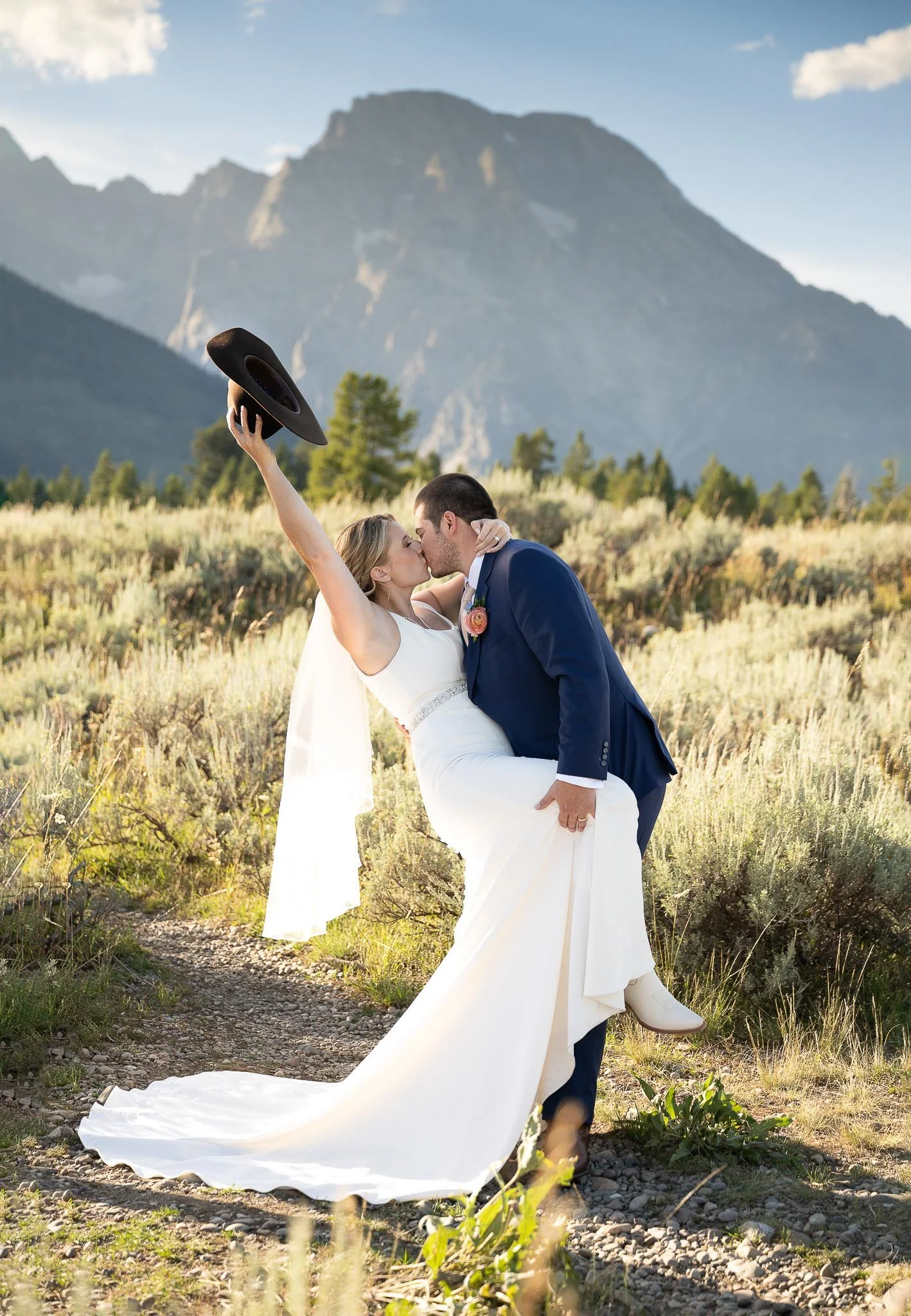 Dramatic mountain dip-kiss with cowboy hat raised overhead, sagebrush foreground, Grand Teton peaks rising in background — Jackson Hole Wyoming wedding photography