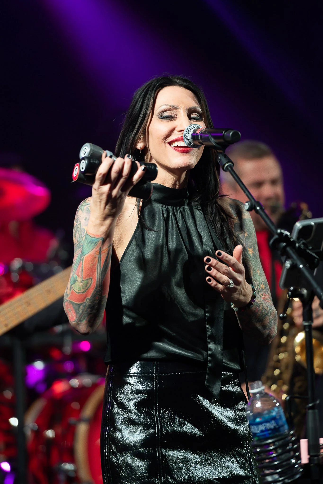 Female performer in dark green halter dress gripping microphone stand, dramatic purple stage lighting and band in background — Milwaukee event band photography