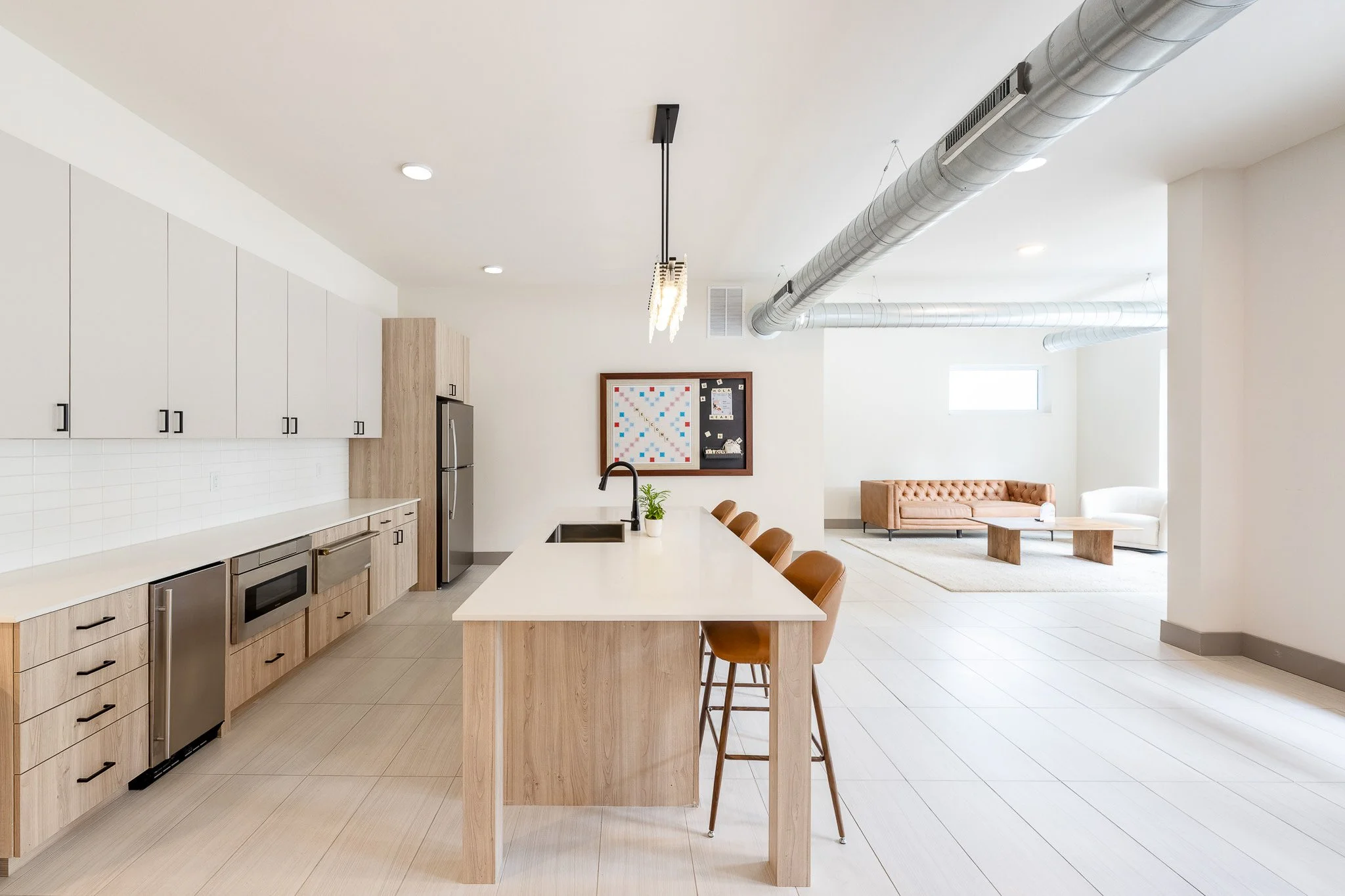 Modern loft apartment common area with light wood kitchen island, white cabinetry, exposed ductwork, and open living space — Milwaukee 1659 Jackson residential interior photography