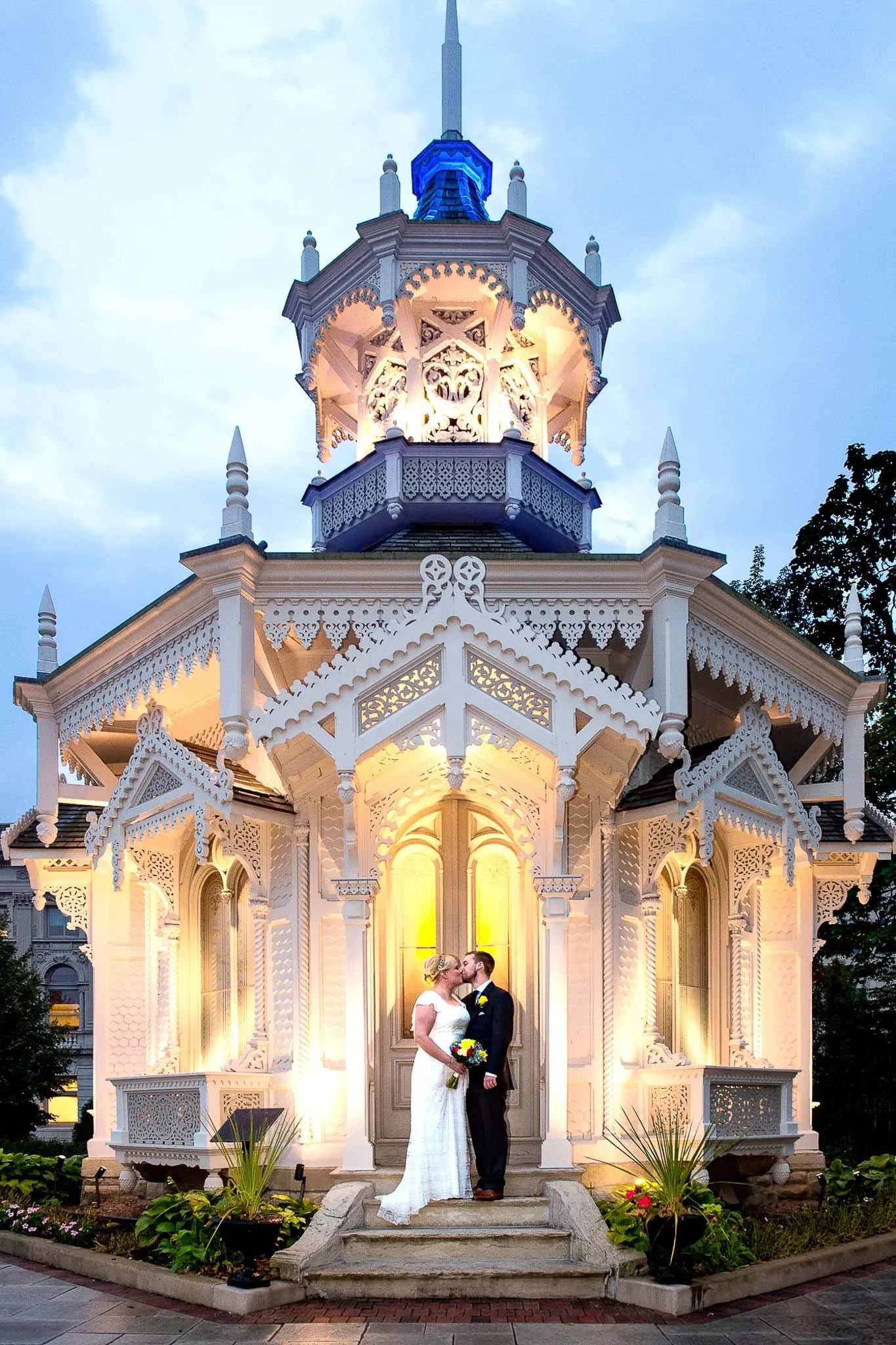 Ornate illuminated Victorian gazebo with blue dome top glowing at dusk, couple sharing a kiss on the steps — Milwaukee wedding photography
