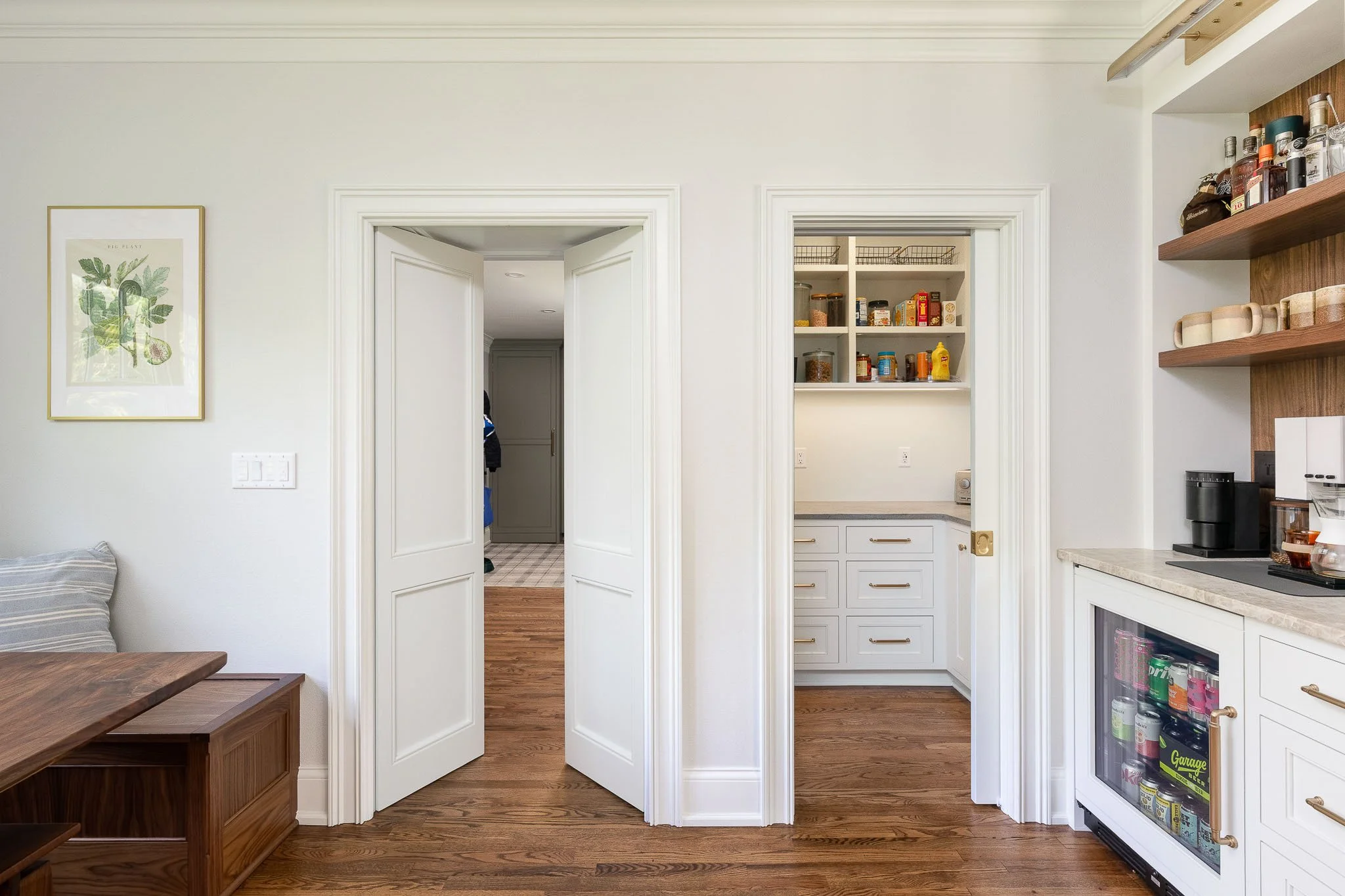 Open mudroom entry showing walk-in pantry with shelving, beverage refrigerator, and adjacent bar cabinetry with floating walnut shelves — Milwaukee  residential interior photography