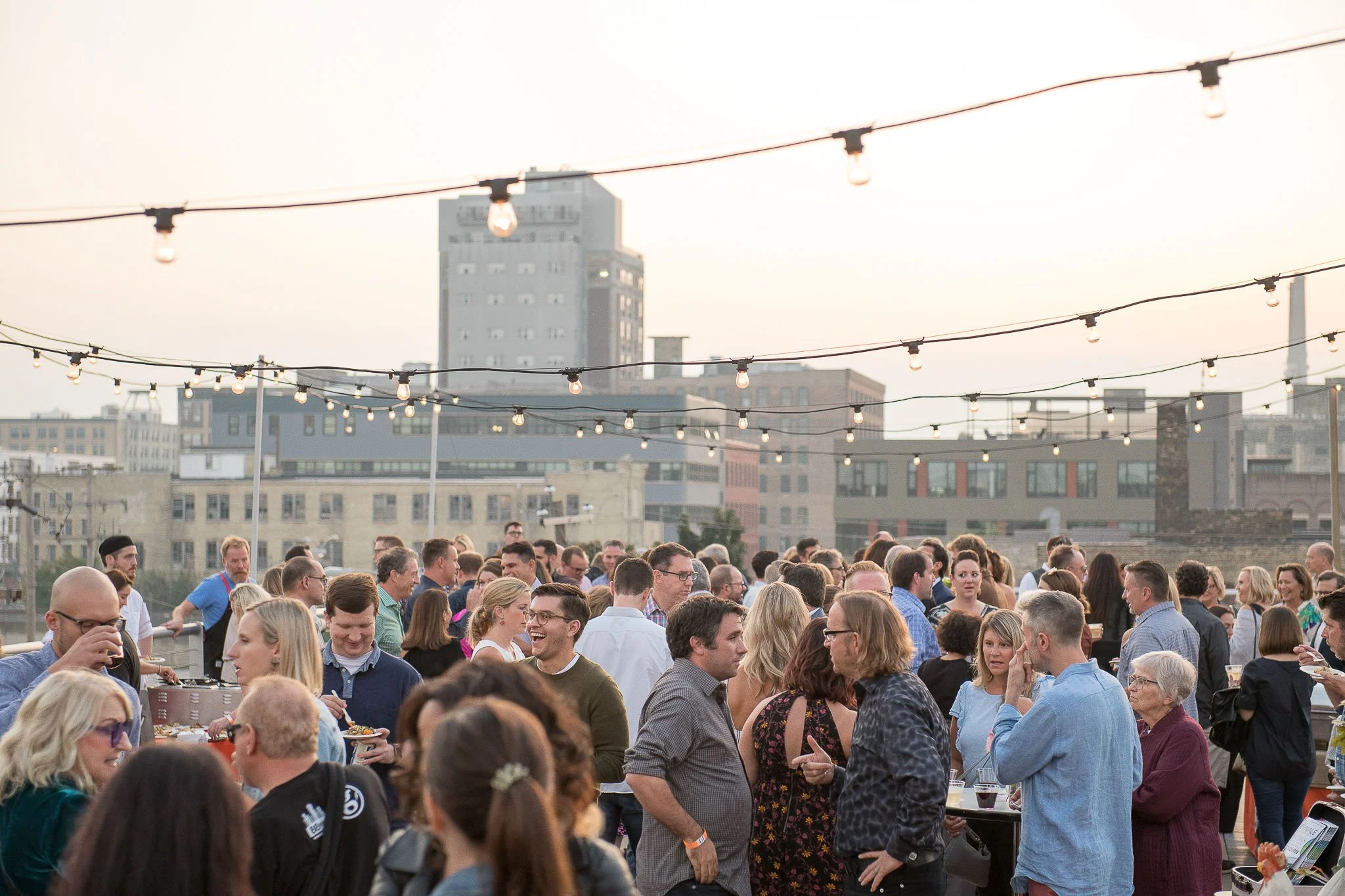 Outdoor rooftop event crowd mingling under string lights against Milwaukee downtown building skyline at dusk — Milwaukee 88Nine Radio event photography