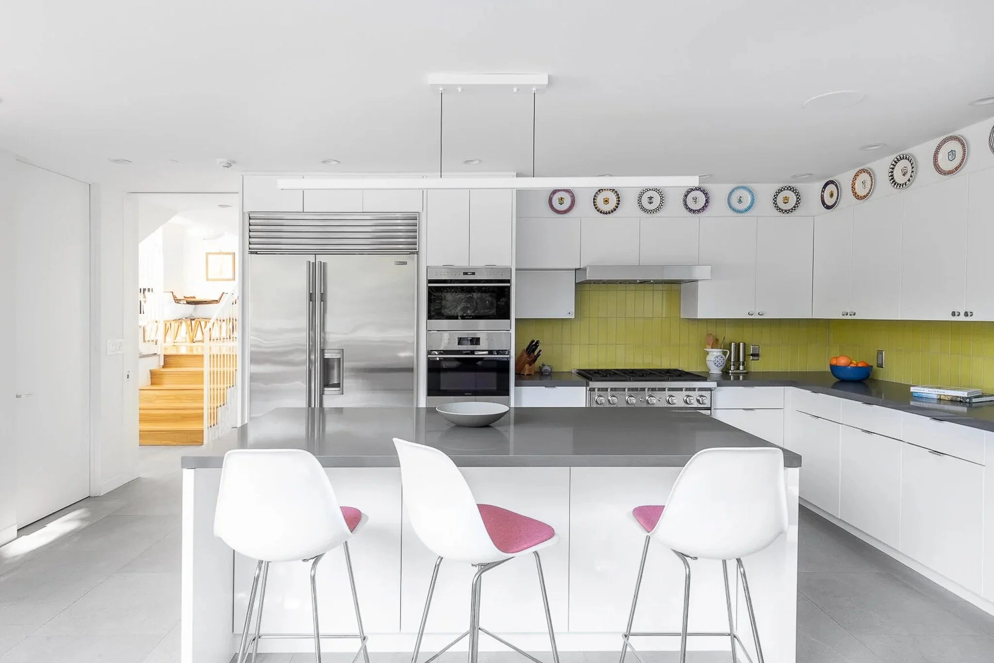 Modern white kitchen with lime green tile backsplash, white tulip bar stools, grey countertops, and stainless Sub-Zero refrigerator — California modern residence interior photography