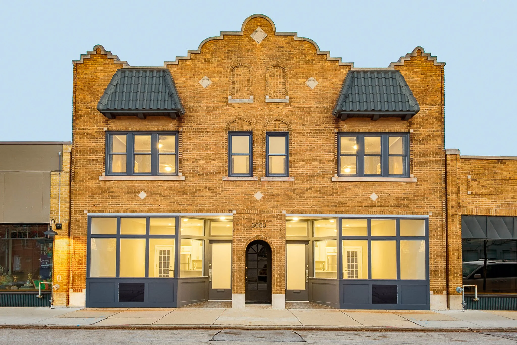 Renovated historic golden brick commercial building at 3050 Delaware with ornamental facade, dark grey window frames, and illuminated storefront at dusk — Milwaukee commercial architecture photography