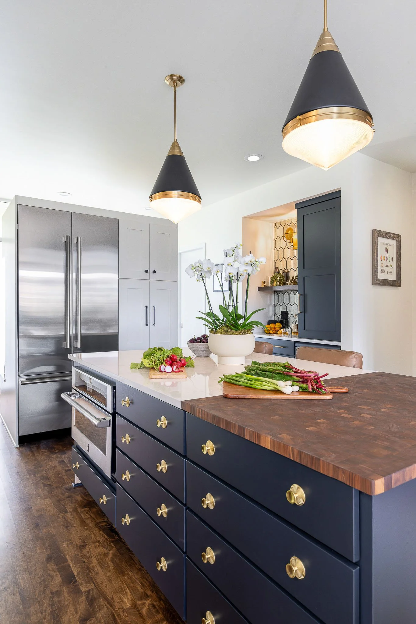 Dark navy kitchen island with brass hardware, butcher block accent, black cone pendants, and open bar alcove — Milwaukee Story Hill residential interior photography