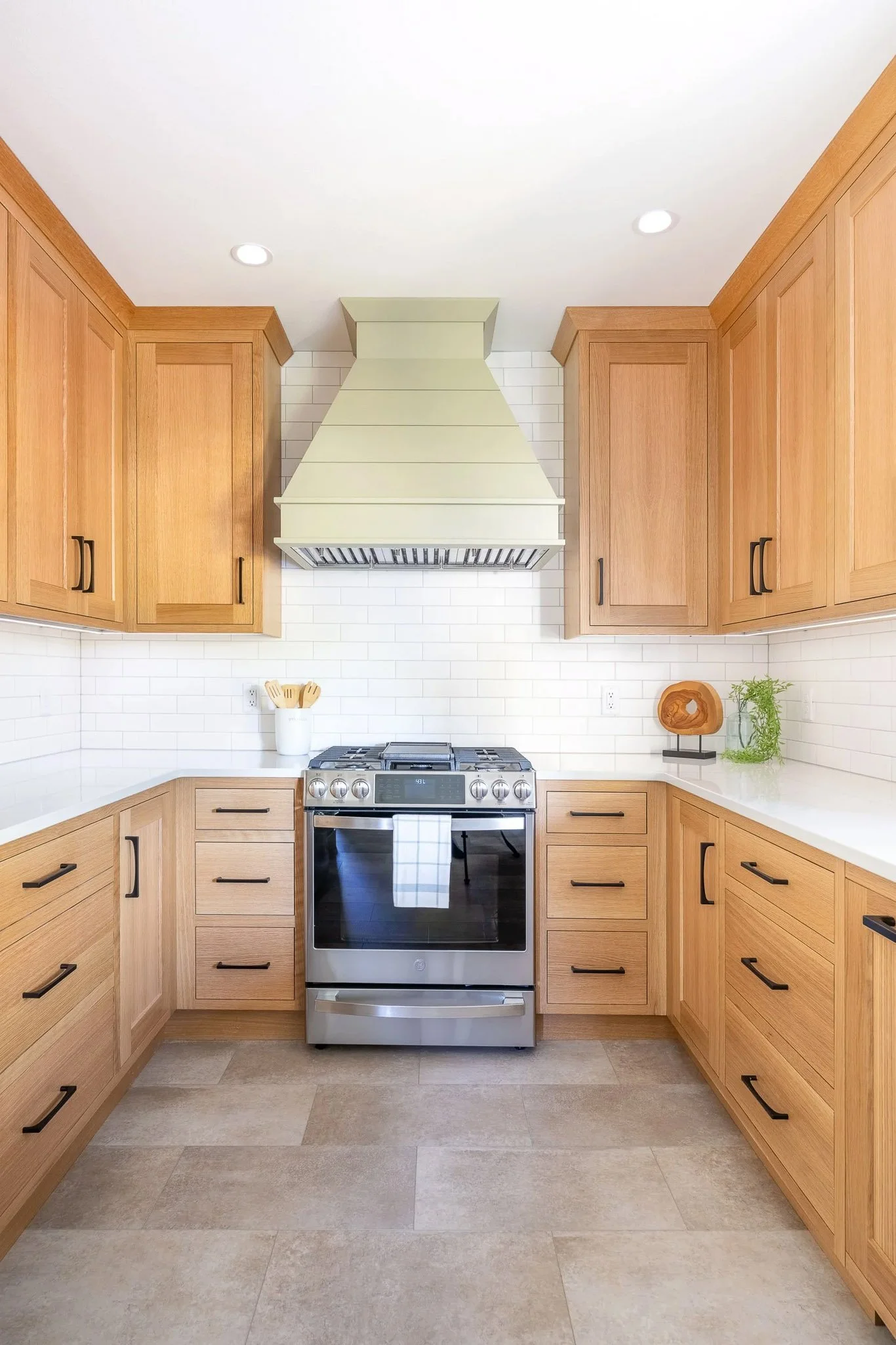 Light oak kitchen with green range hood, black hardware, stainless slide-in range, and grey tile floor — Milwaukee residential interior photography
