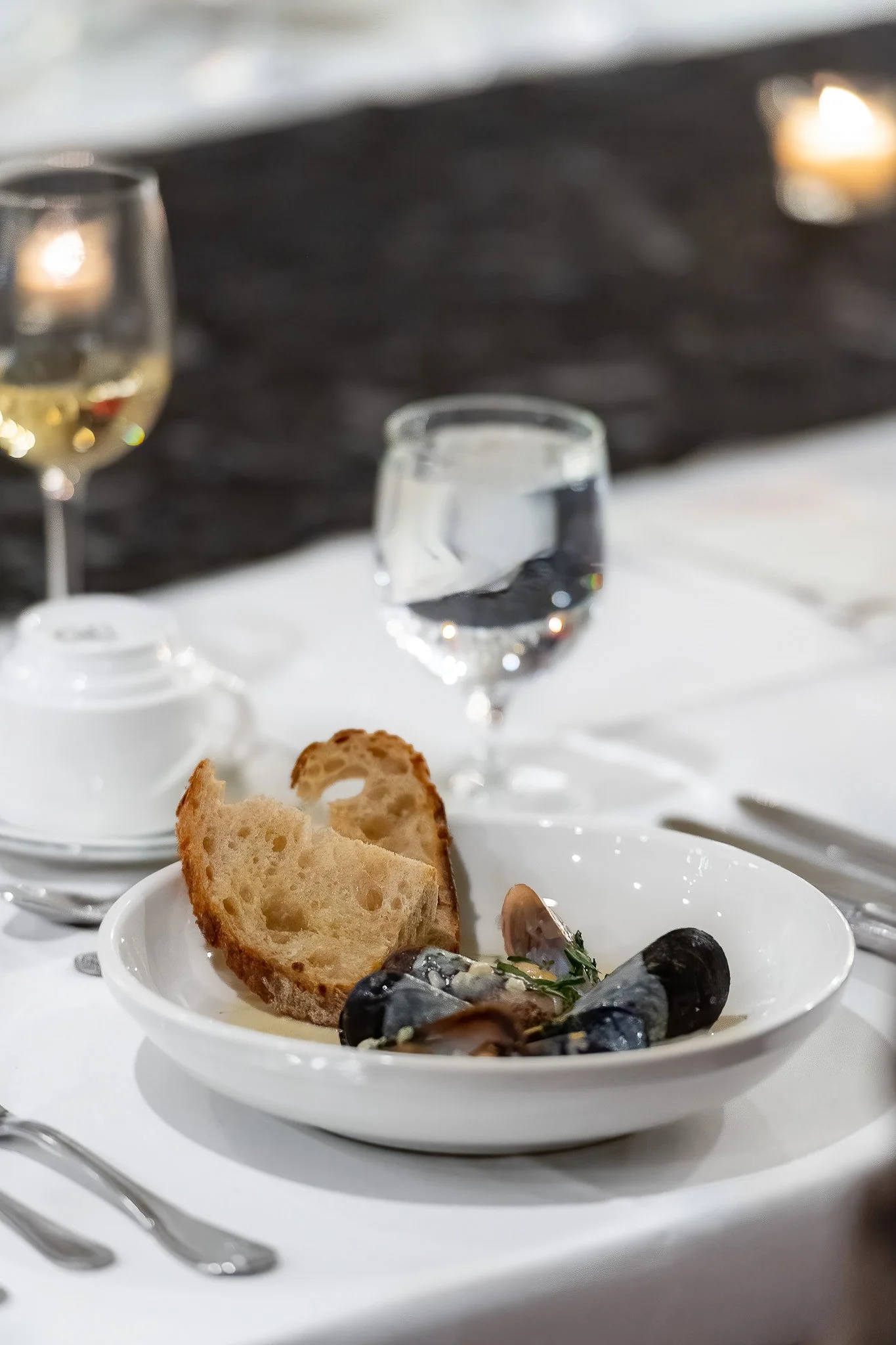 Elegant plated mussel dish with artisan bread on white linen tablecloth, wine glass in background — Milwaukee fine dining event photography