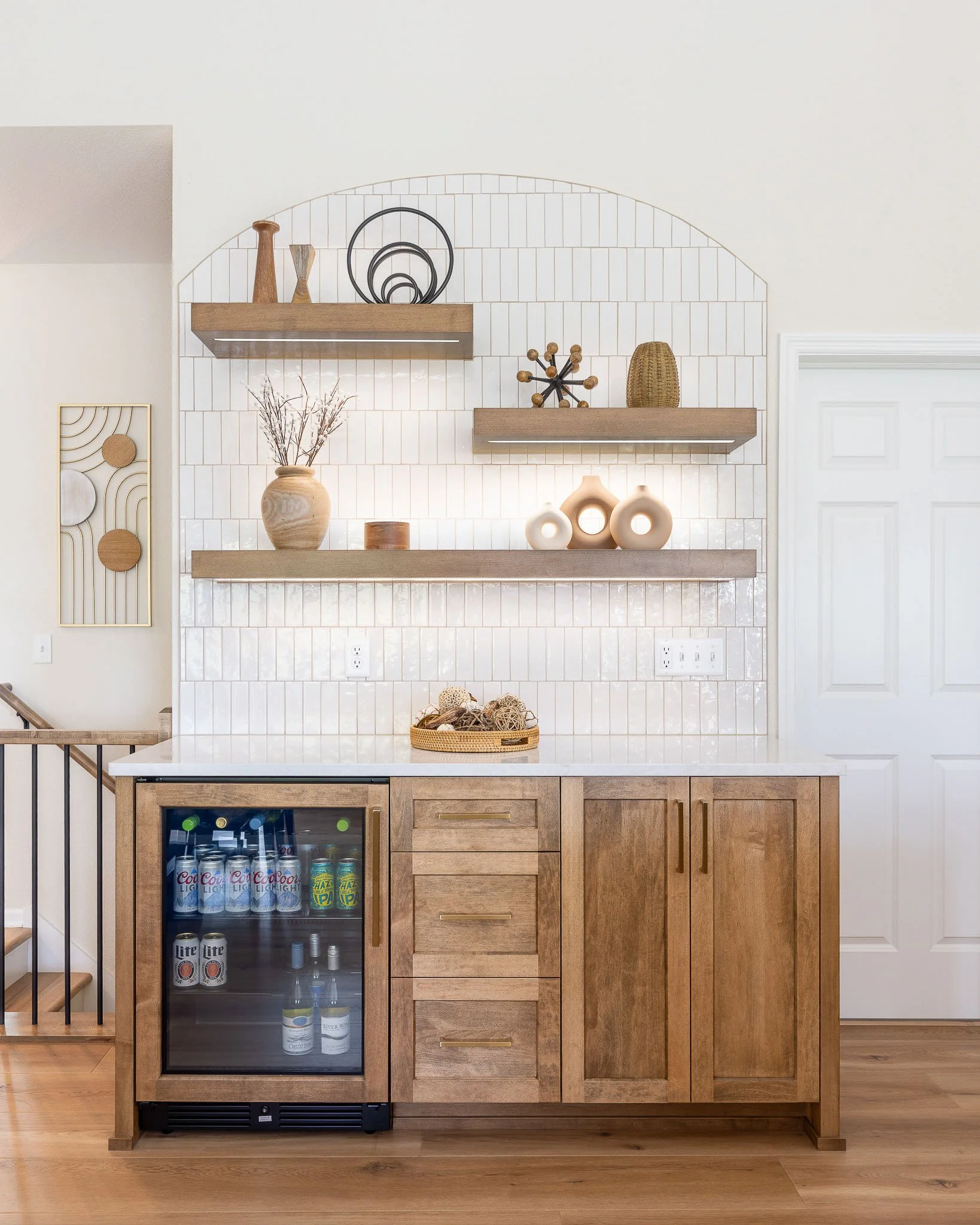 Warm wood butler's pantry with arched white subway tile backsplash, floating wood display shelves, beverage refrigerator, and brass hardware — Milwaukee residential interior photography
