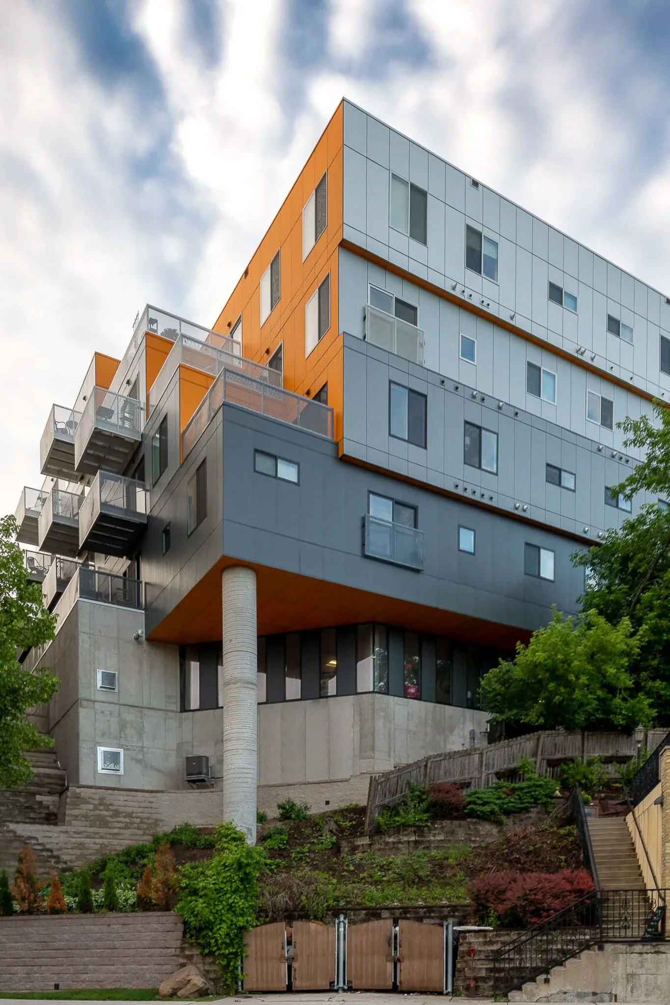 Bold orange and grey cantilevered apartment building rising from a landscaped hillside — Milwaukee Nine10 residential architecture photography