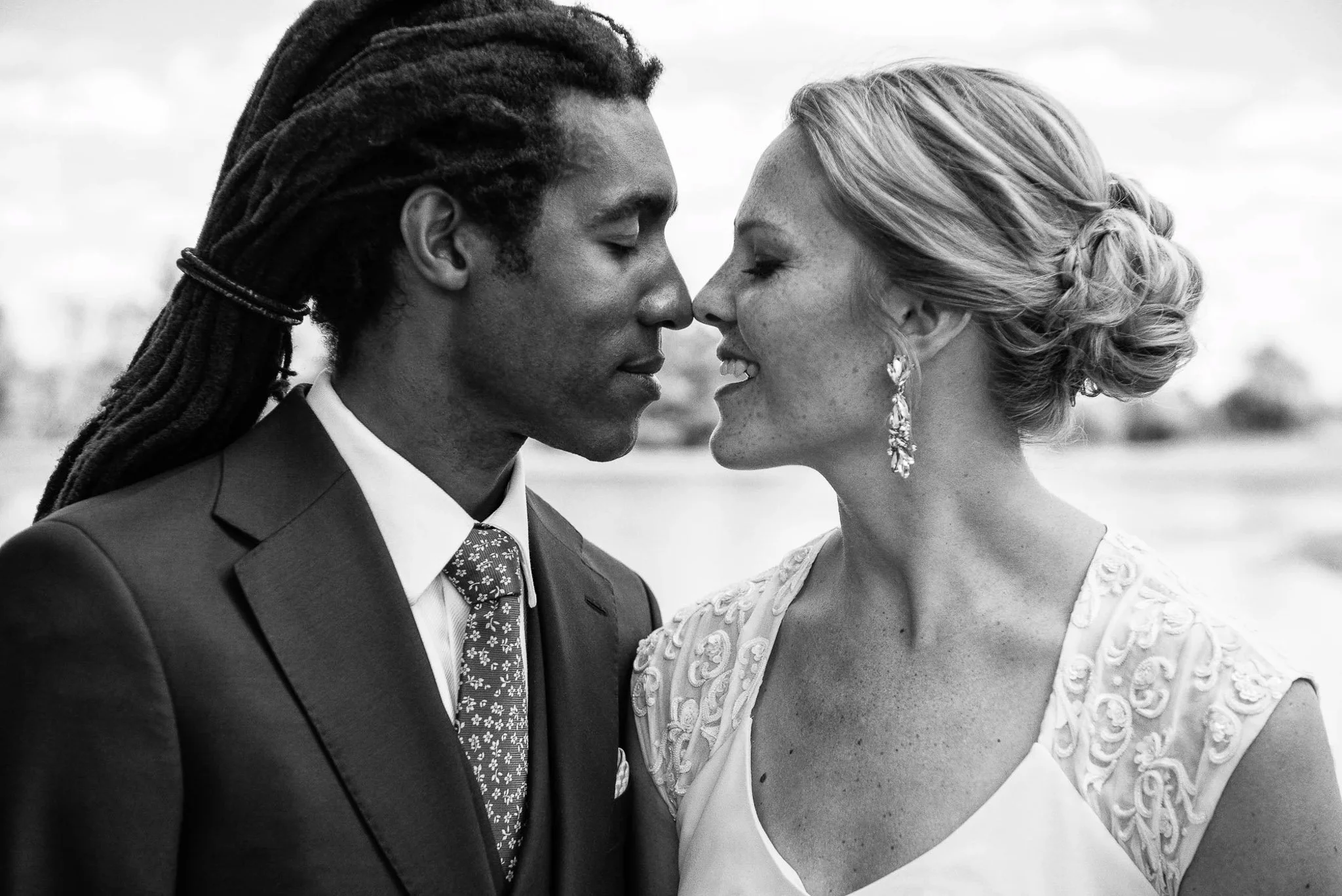 Black and white intimate portrait of couple nearly kissing, groom with dreadlocks in dark suit with floral print tie, bride in beaded cap-sleeve gown with elegant updo — Milwaukee wedding photography