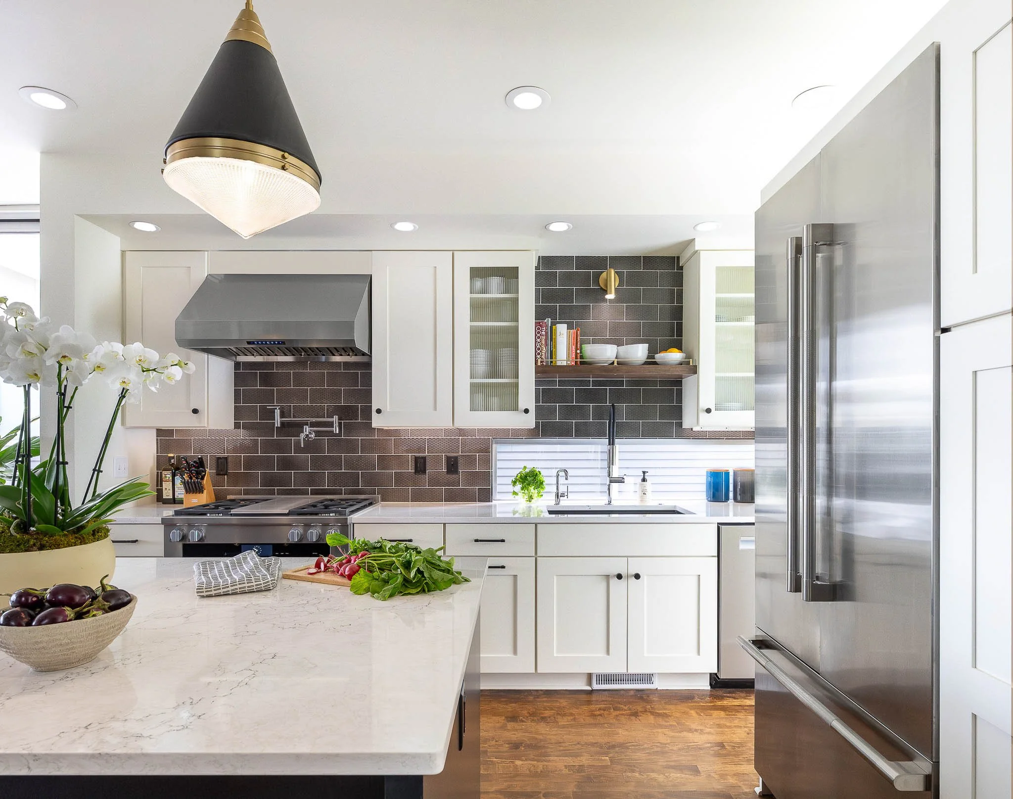 White kitchen with dark grey tile backsplash, marble countertops, black and gold cone pendant, and stainless Sub-Zero refrigerator — Milwaukee Story Hill residential interior photography