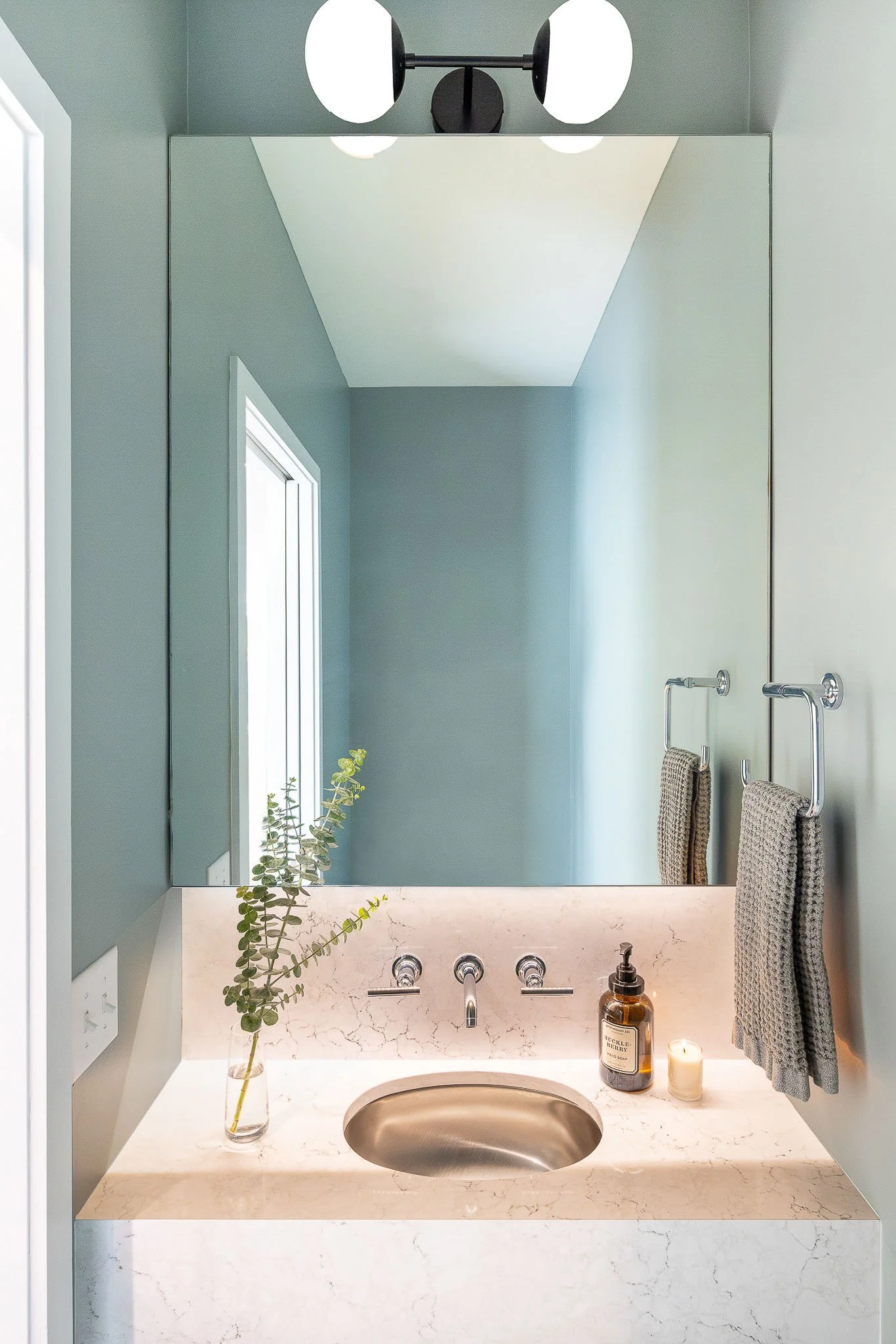 Teal and sage powder room with round undermount sink, wall-mount faucet, and eucalyptus stem in vase — Milwaukee Story Hill residential interior photography