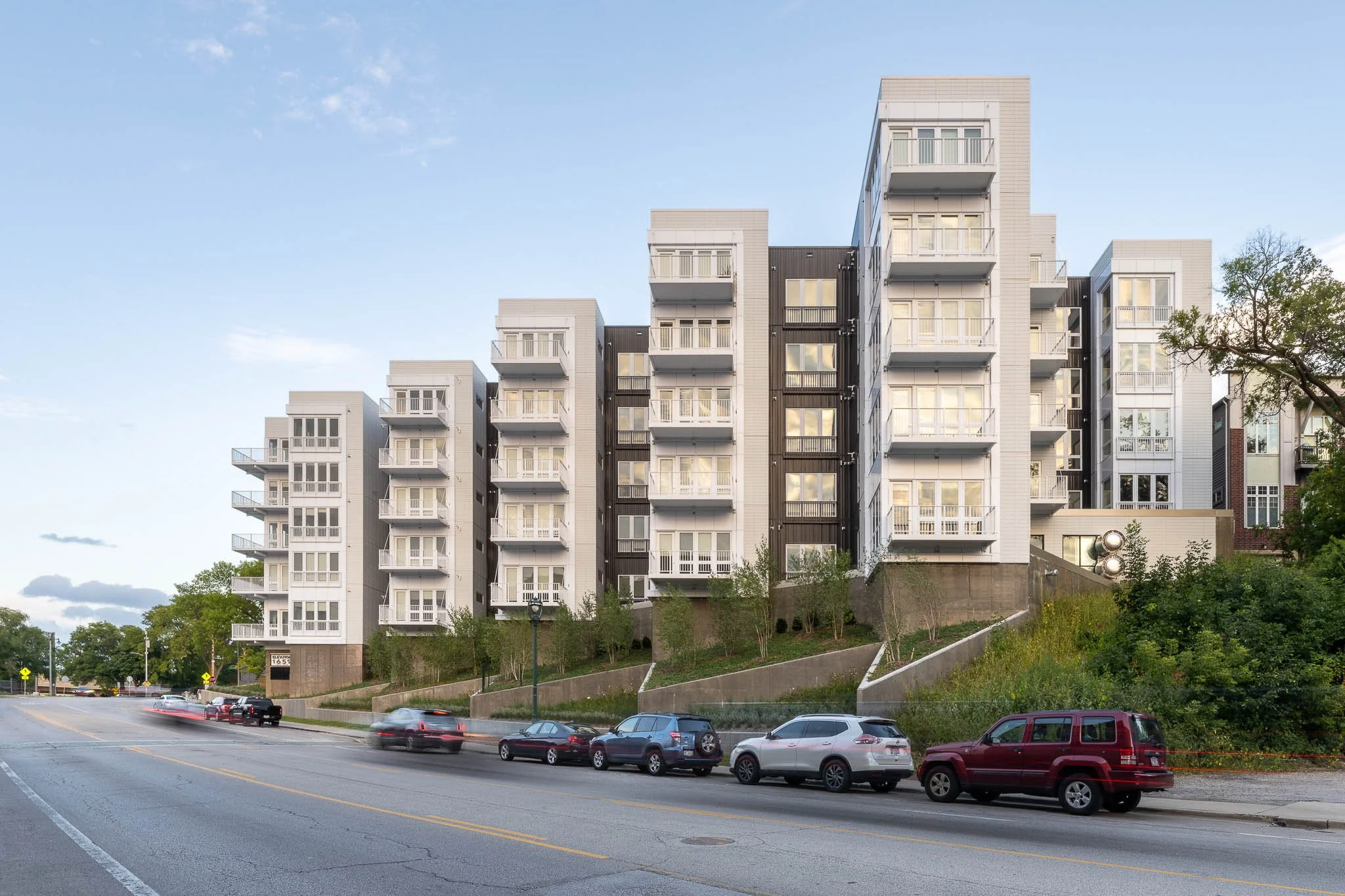Wide street-level view of modern white apartment complex with staggered balconies along arterial road at dusk — Milwaukee 1659 Jackson residential architecture photography