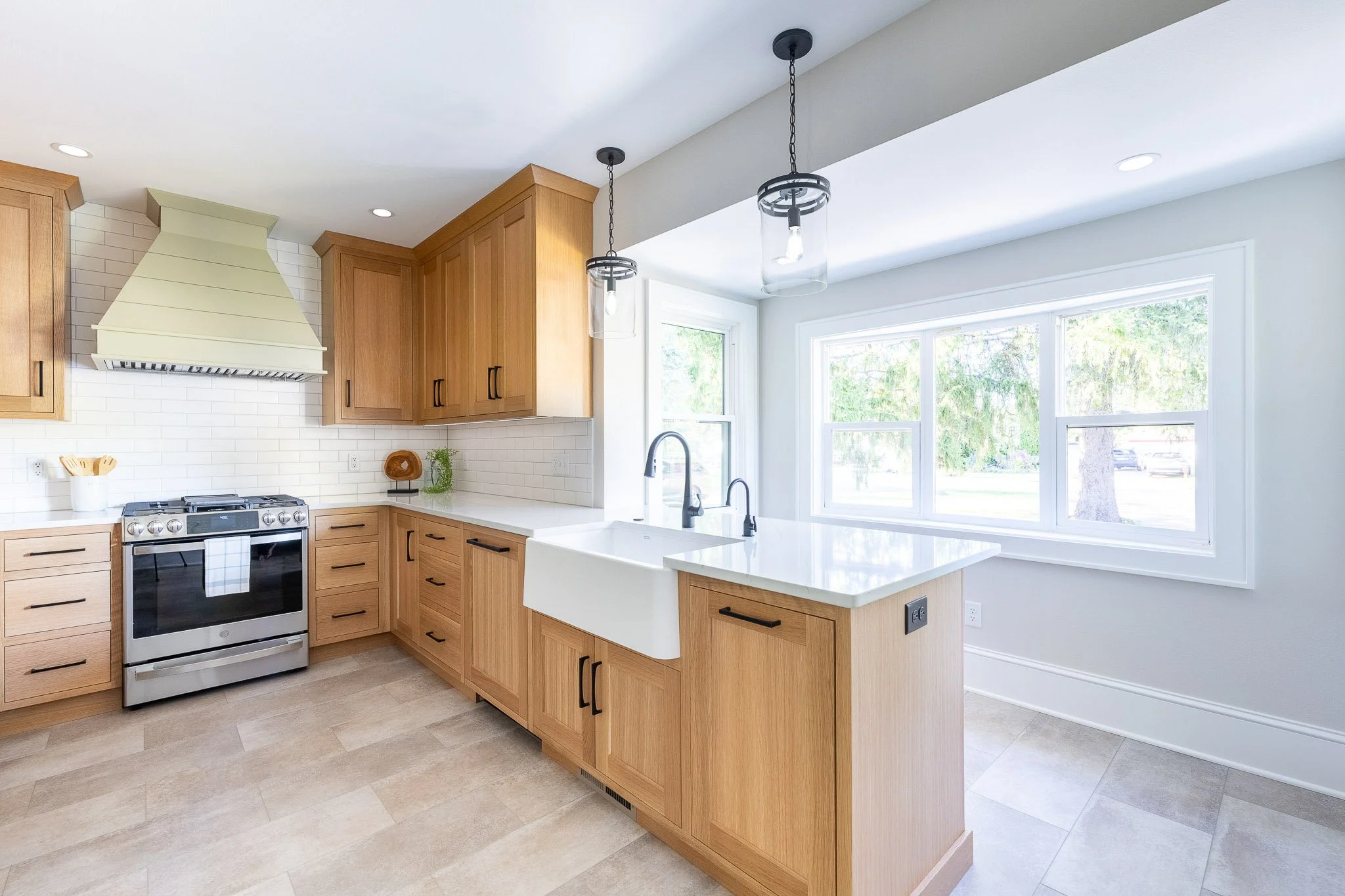Light oak kitchen with green range hood, black hardware, stainless slide-in range, and grey tile floor — Milwaukee residential interior photography