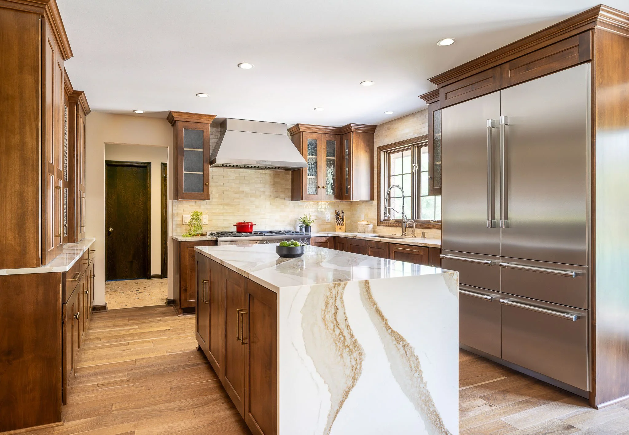 Dark walnut kitchen with dramatic white marble waterfall island, gold veining, stainless Sub-Zero refrigerator, and stone tile backsplash — Milwaukee residential architecture photography