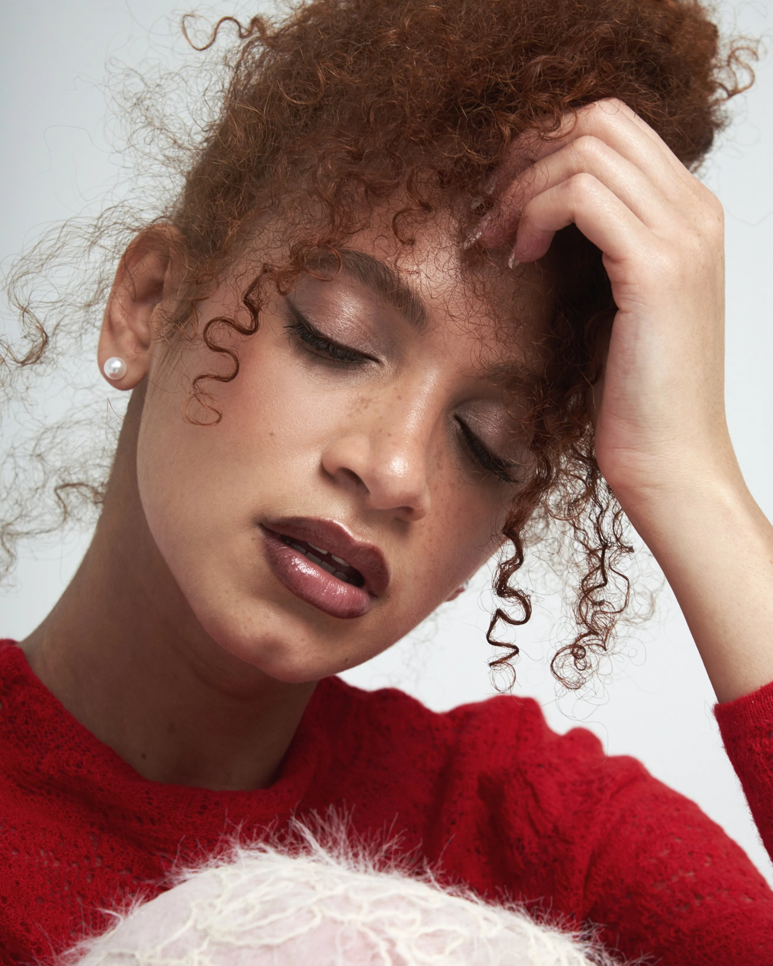 Model with light coverage foundation for medium skin tone, brown reddish glossy overlined lips, soft brown eyeliner, light bronzer and blush makeup.