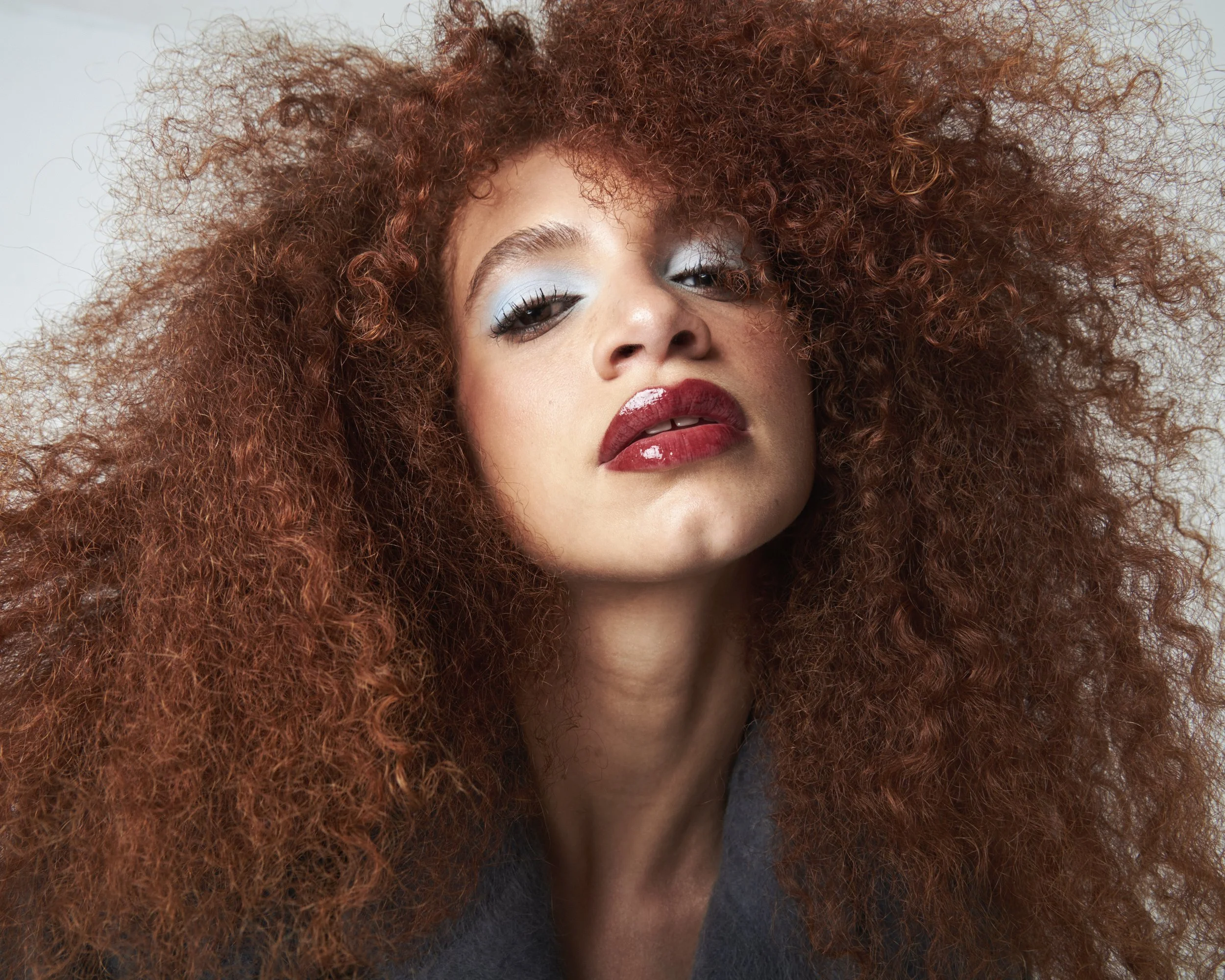 Model with light coverage makeup for medium skin tone, baby blue cream eyeshadow, bold red glossy lip, berry lip liner.