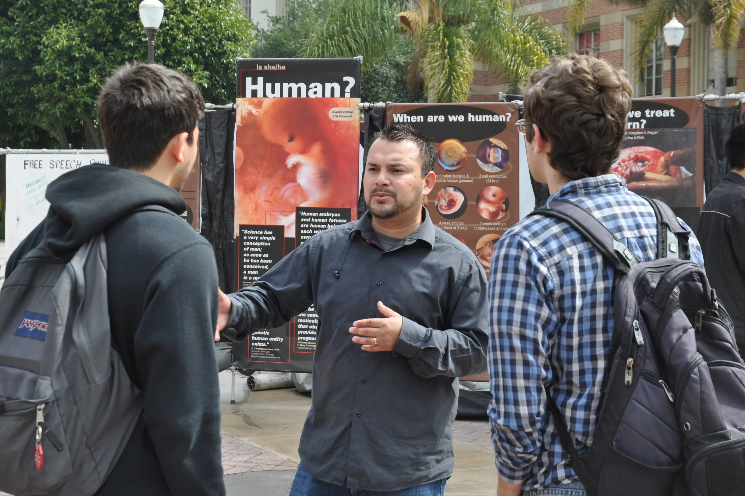 Marcos Espinoza (center), a staff member with Right to Life of Central California, interacts with UCLA students in front of the JFA Exhibit on Bruin Plaza.