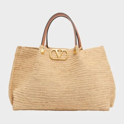 A beige knitted tote bag with two brown handles and gold hardware, featuring a logo at the top center.