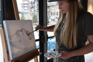 Woman painting on an easel near a large window during a private art experience