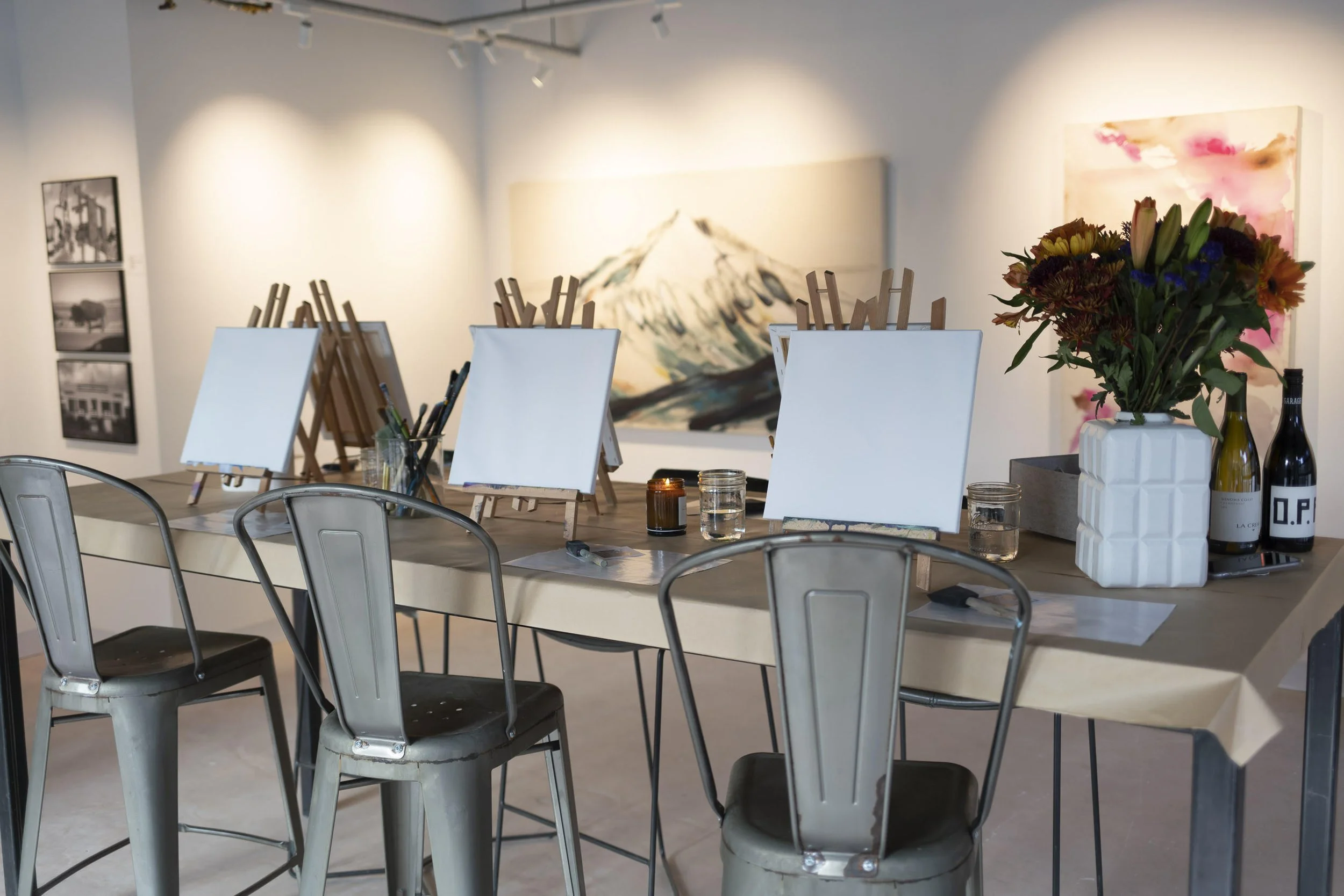 Studio space with blank easels and chairs set up for an art experience class, with a large mountain painting on the wall