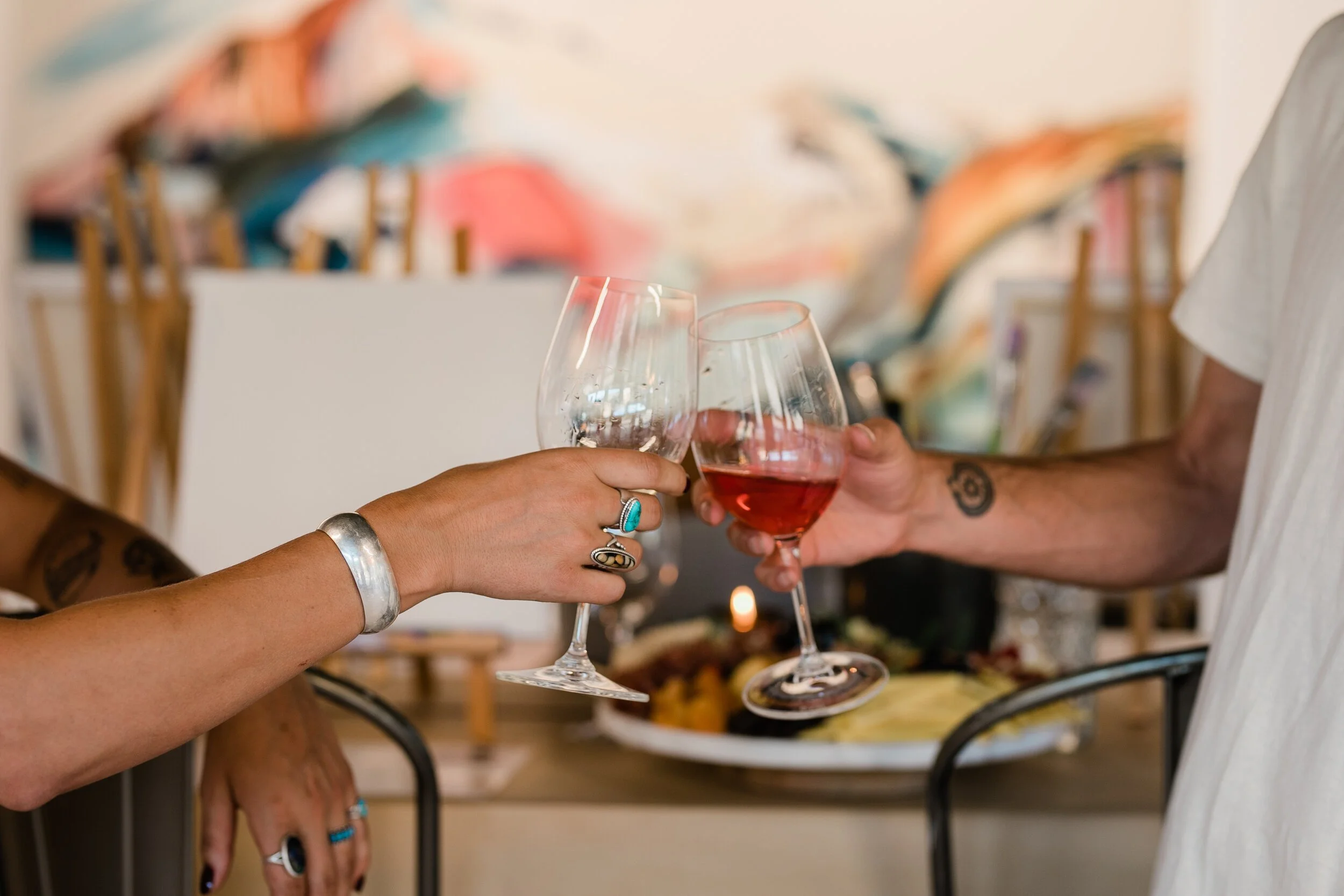 Two hands clinking wine glasses at a Kelly Peters art experience event