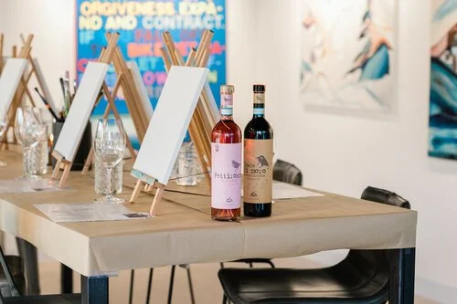 Wine bottles and a blank canvas on a table set up for a Kelly Peters art experience