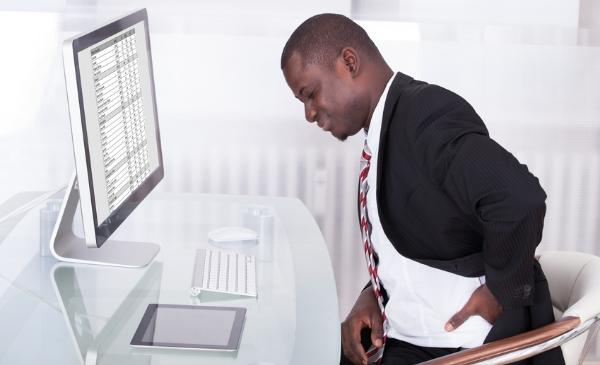 Man experiencing lower back and neck pain while sitting at a desk with poor posture – common issue treated with therapeutic massage at Massage Hope in Leesburg and Ashburn VA