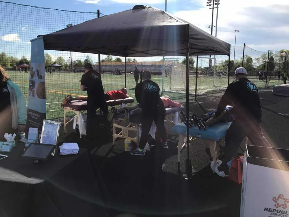 Massage therapists providing sports recovery and athletic massage under a tent at a community sports event on a field in Loudoun County – Massage Hope supporting local athletes in Leesburg and Ashburn VA