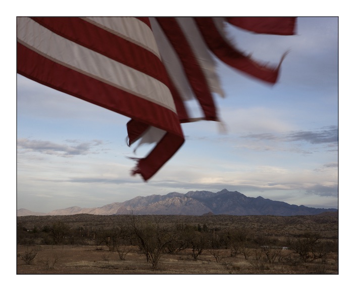  A US flag tethered to a family gatepost flutters in the afternoon breeze on the road between Arivaca and Amado, in the background is the Santa Clara mountain range. 