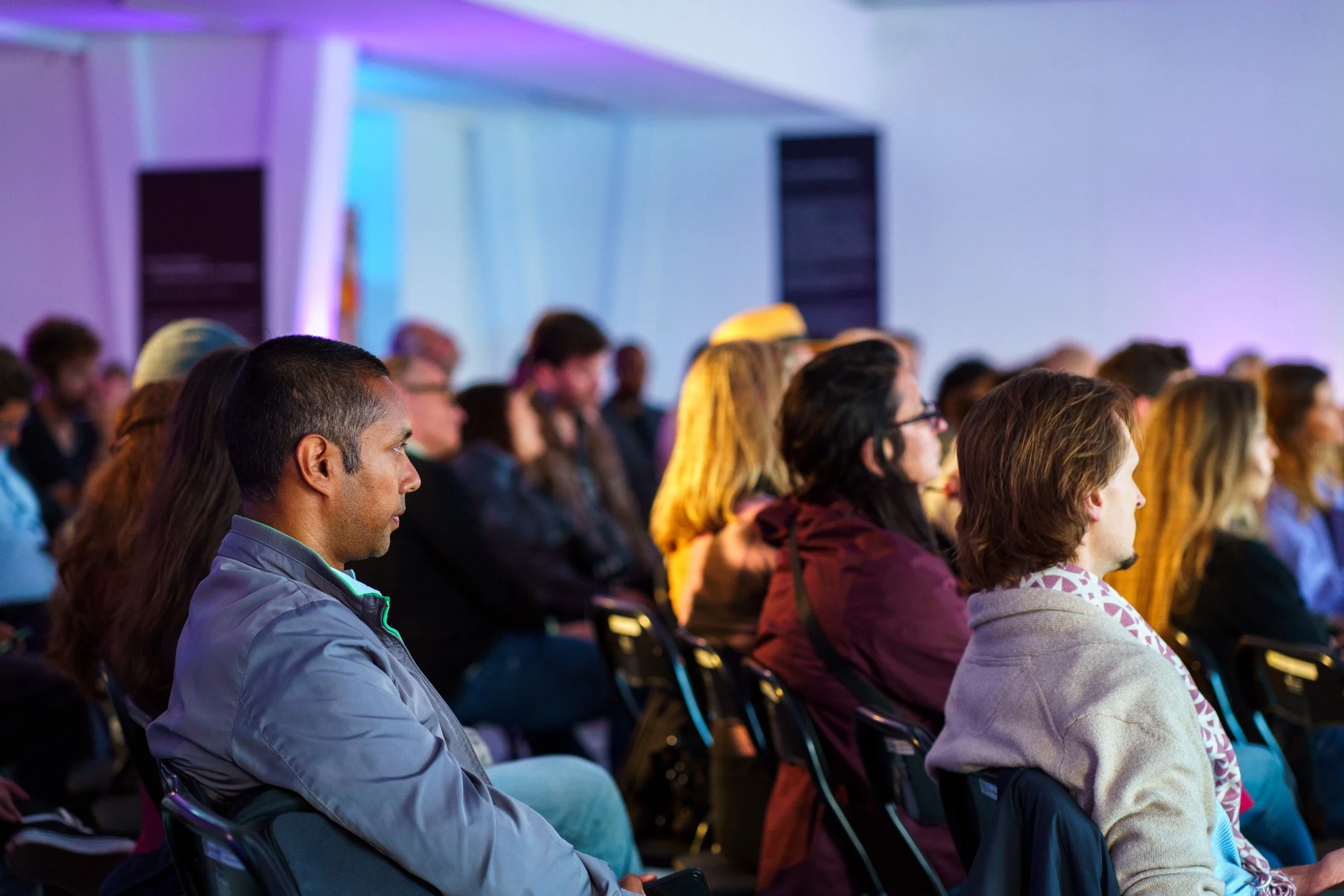 Audience members sitting in rows during a conference or presentation, focused on the speaker or stage.