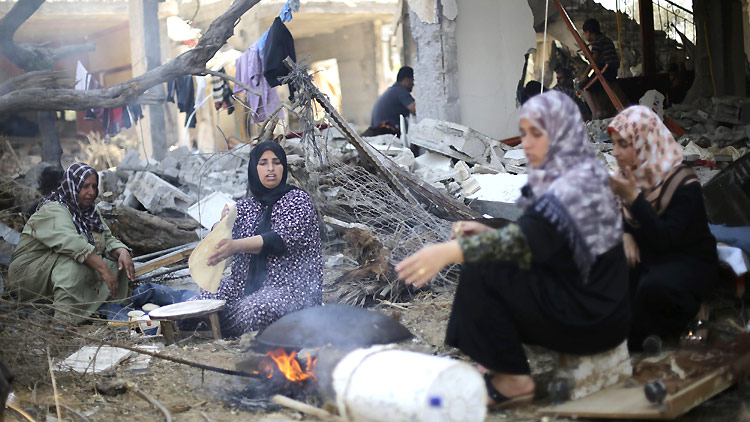 August 14: Palestinian women bake bread in front of the remains of their house in Khan Younis, in the southern Gaza Strip. ©Reuters/I. Abu Mustafa