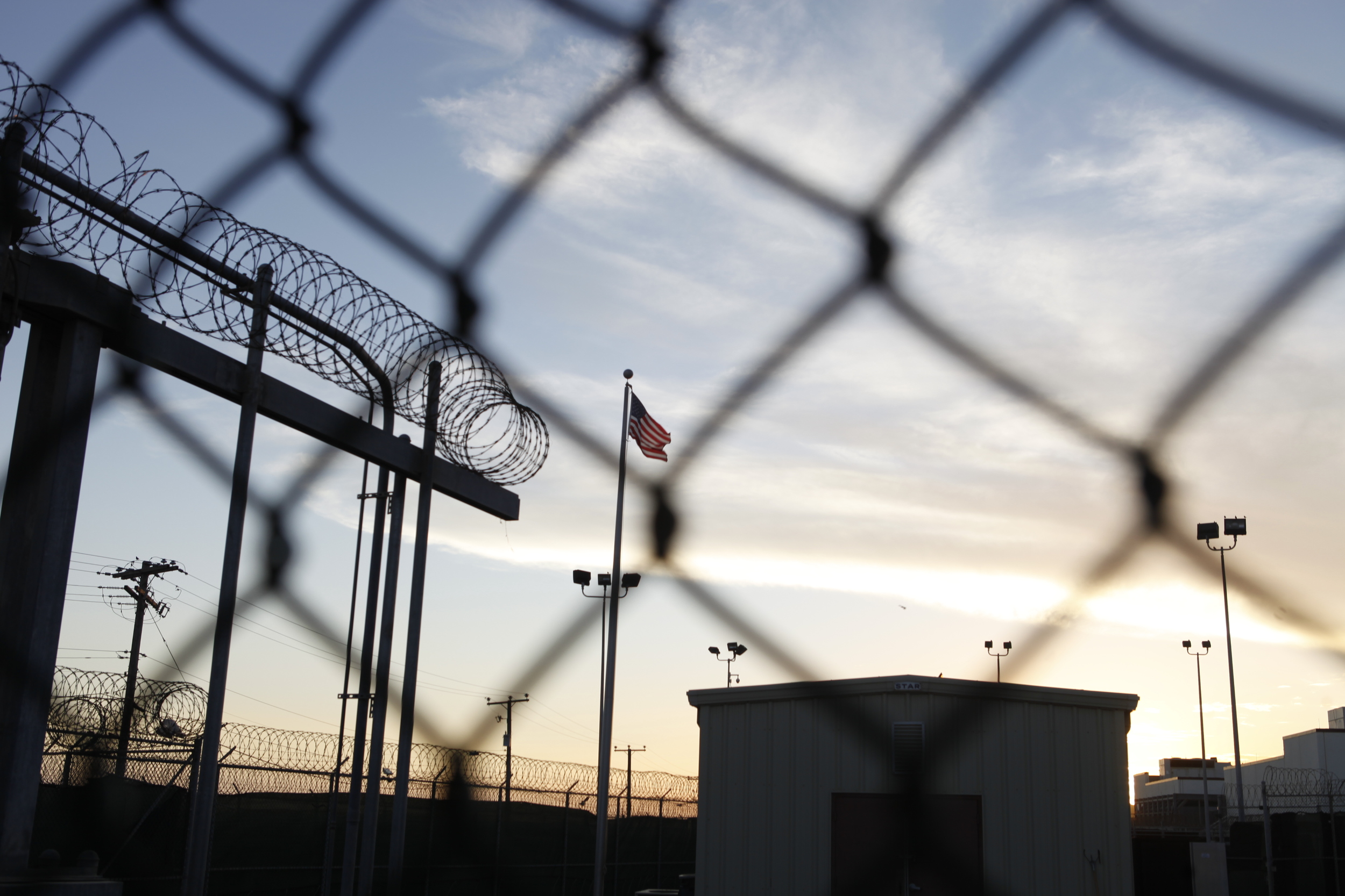February 2014: The American flag can be seen through a barbed wire fence inside Camp 5 as the sun sets on Guantanamo Bay. Copyright: ICRC/Anna Nelson