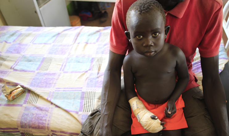 A child with a gunshot wound to his hand rests on his father's lap as he undergoes medical treatment at the general military hospital in Juba, 28 December 2013. © Reuters/James Akena